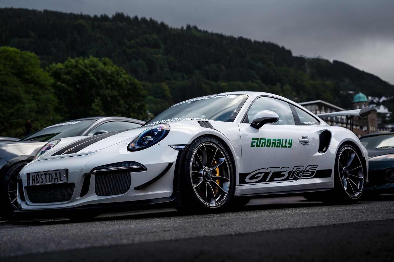 White Porsche GT3 RS with racing livery parked in a lot with mountains visible behind.