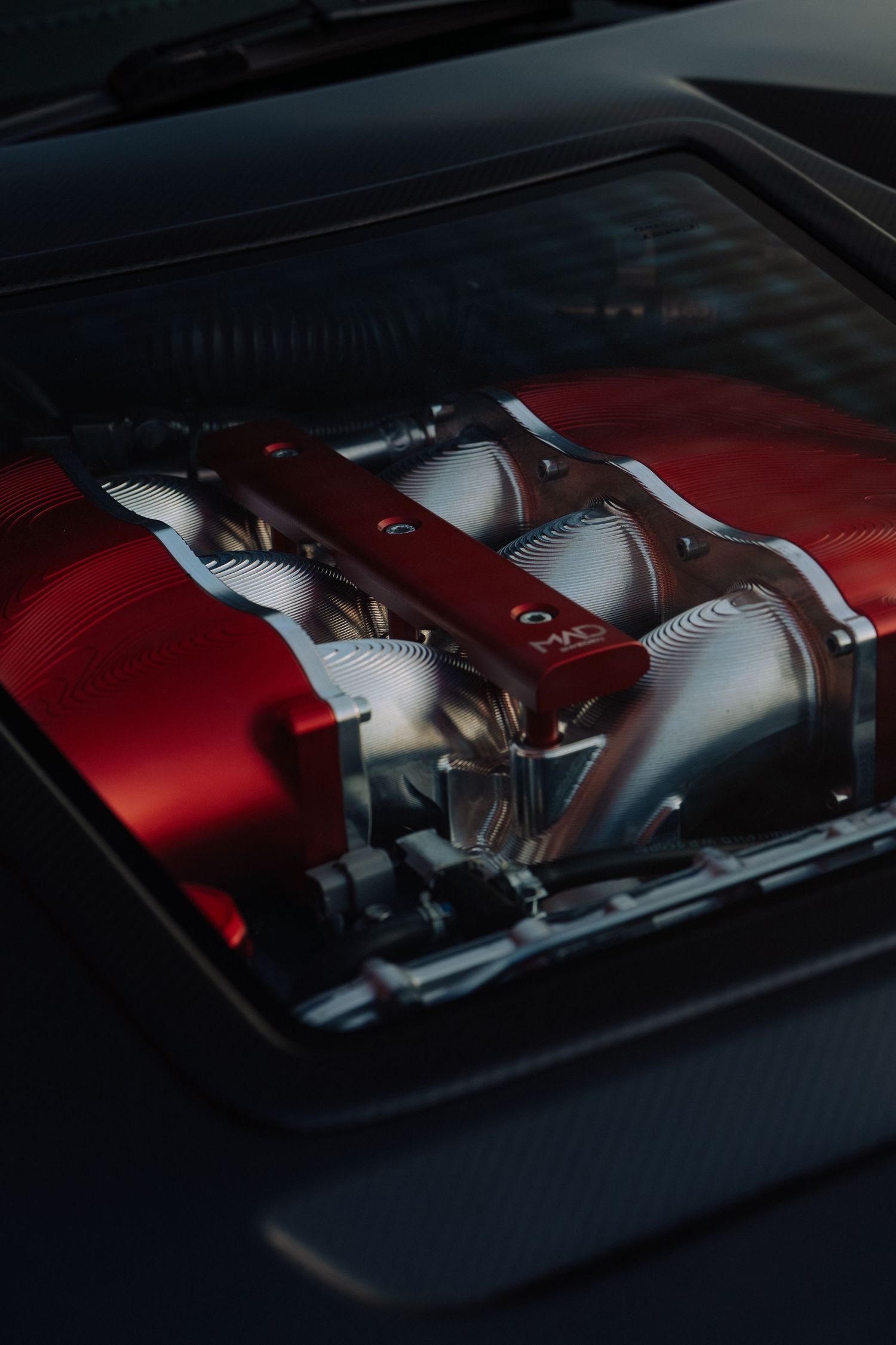 Close-up view of a red engine intake manifold with silver throttle bodies under a car hood.