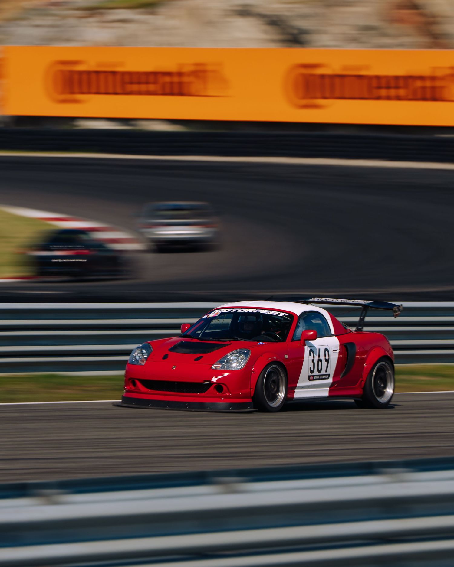 Red racing car speeding along a racetrack at sunset with motion blur effect creating a dynamic action shot.
