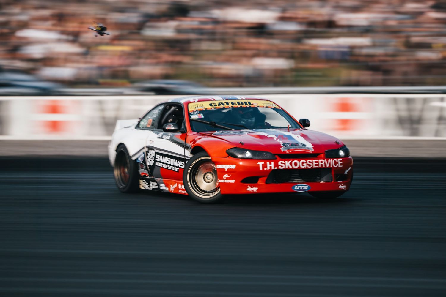 Red drift car sliding sideways on racetrack with motion blur during competitive motorsport event.