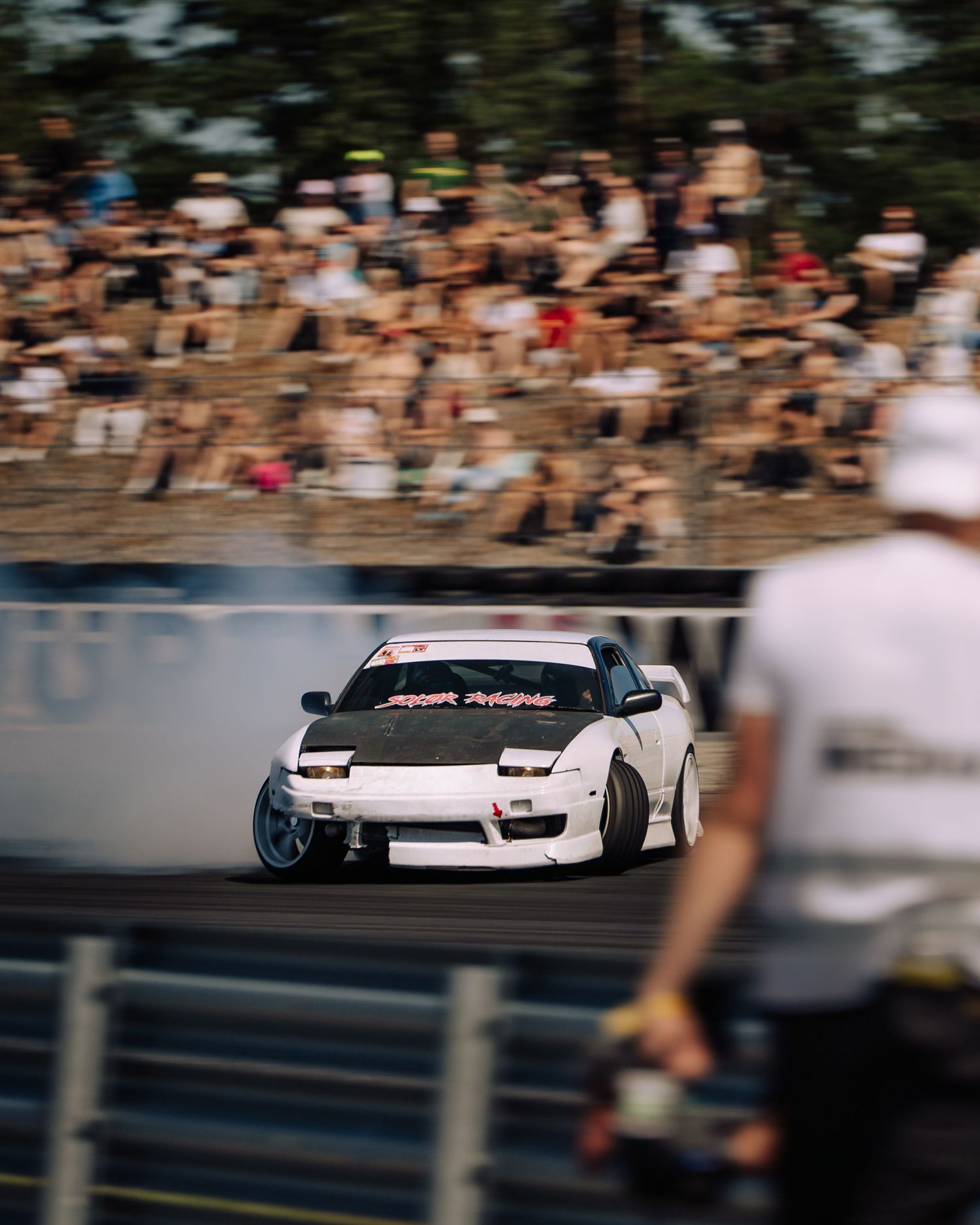 A sequence of racing cars drifting on a track during a motorsport competition with blurred spectators in the background.