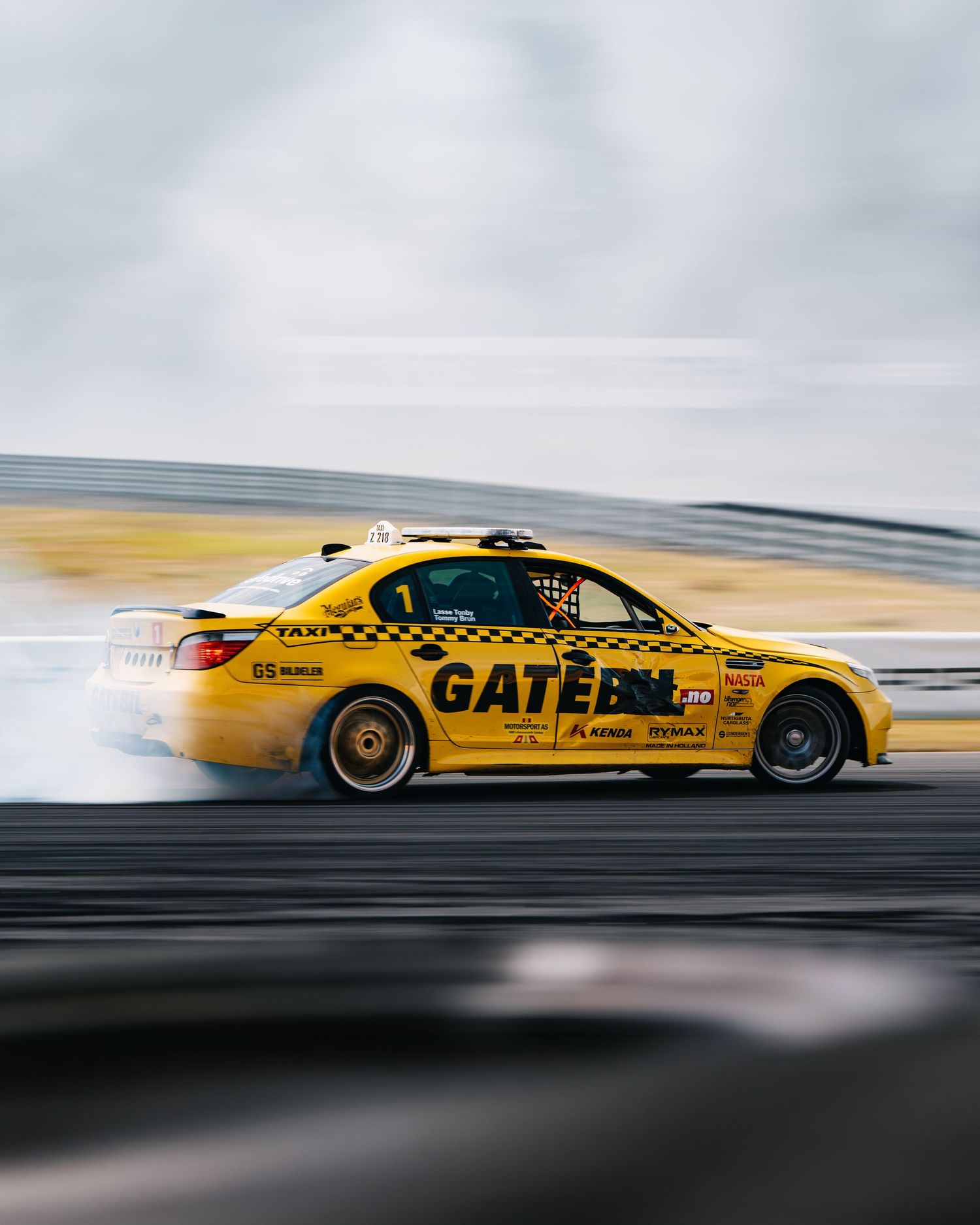 Yellow racing car drifting on a track with motion blur, showcasing dynamic motorsport action.
