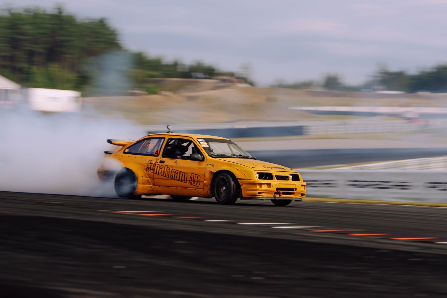 Yellow sports car drifting on a race track creating smoke from burning rubber during a motorsport competition.