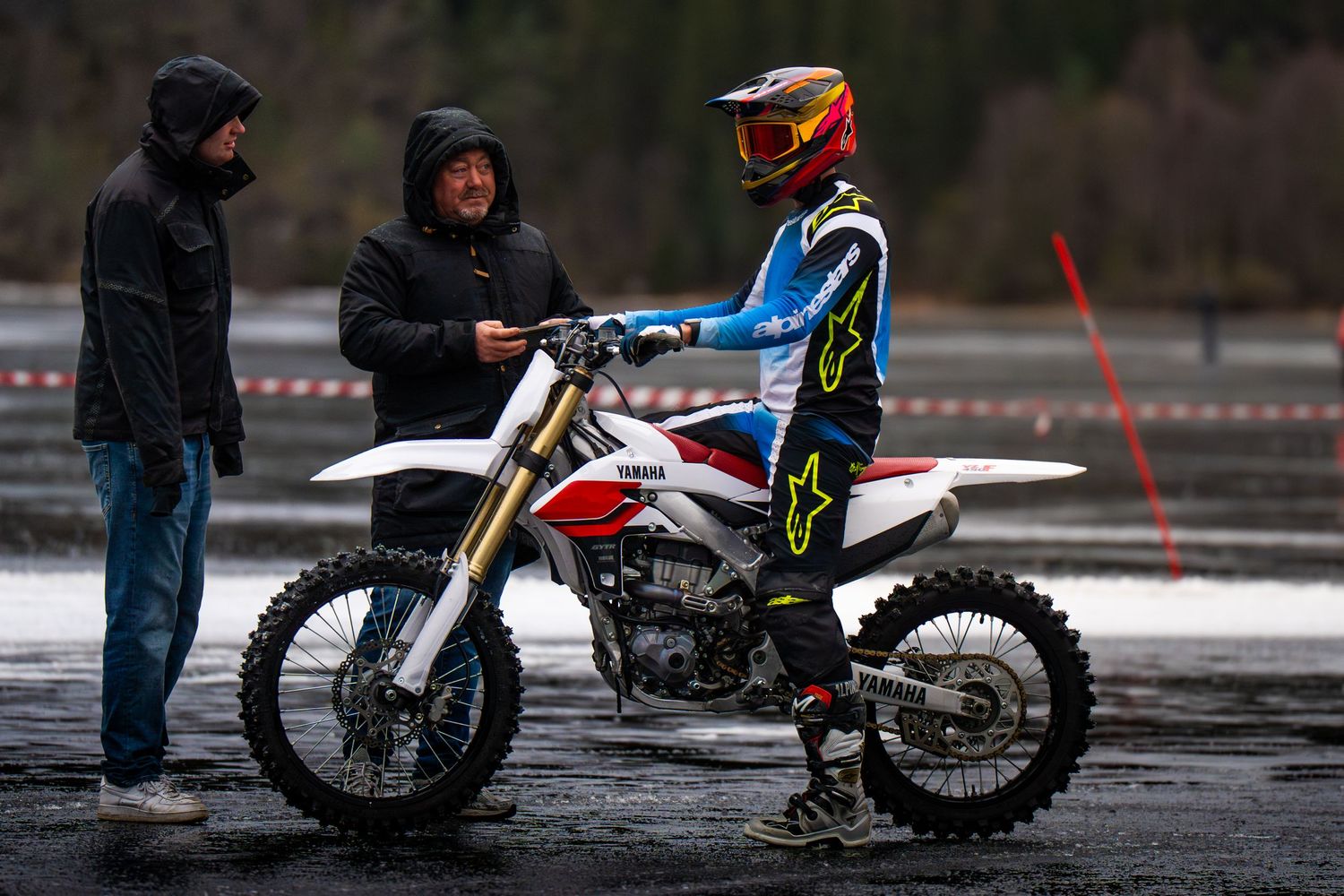 Motocross riders racing on a wet track during a rainy competition event.