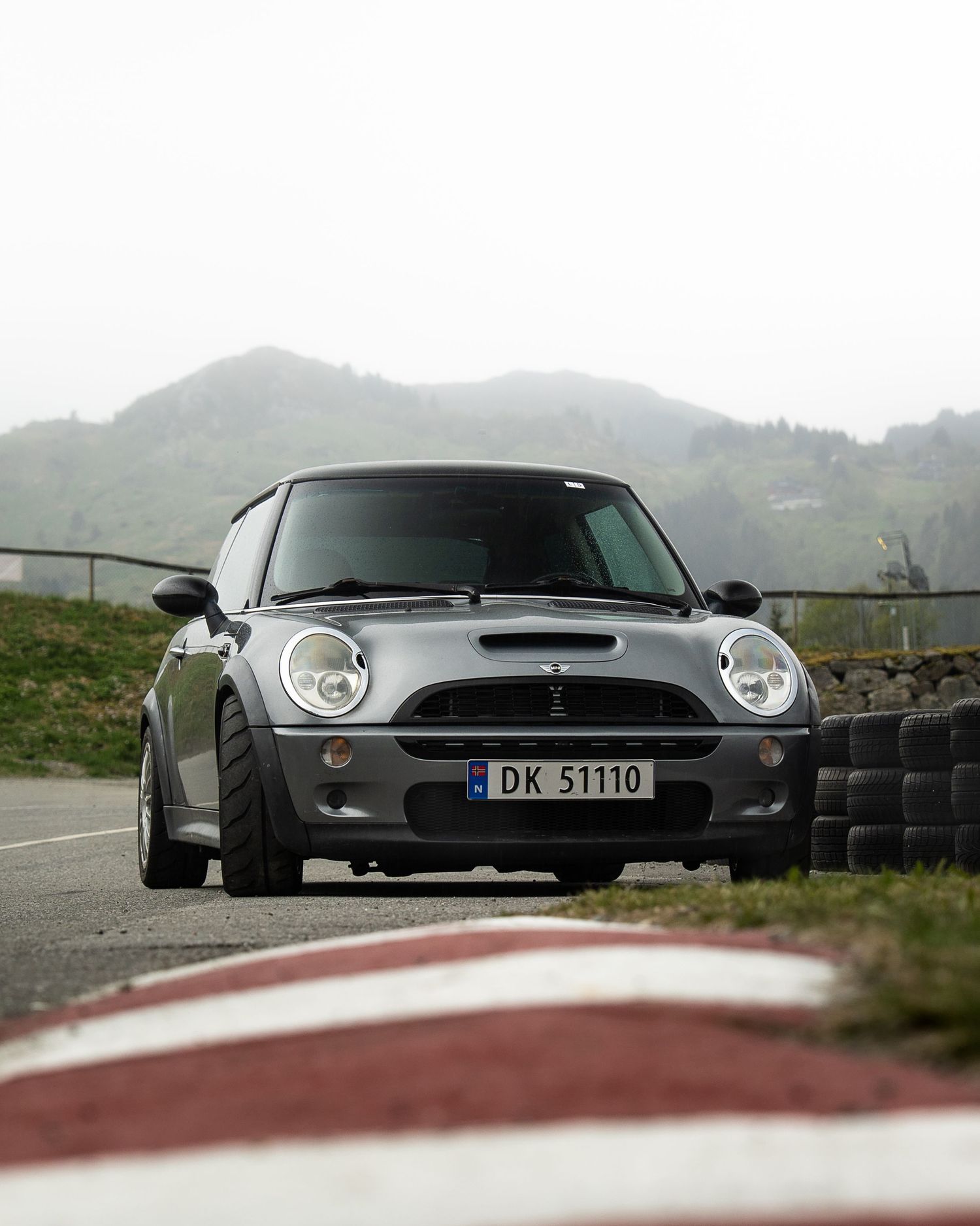 A sleek black Mini Cooper photographed from different low angles on a curving mountain road with misty scenery.