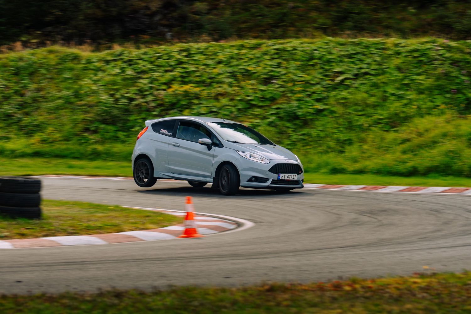 A series of cars navigate a winding mountain road with lush green scenery in the background.