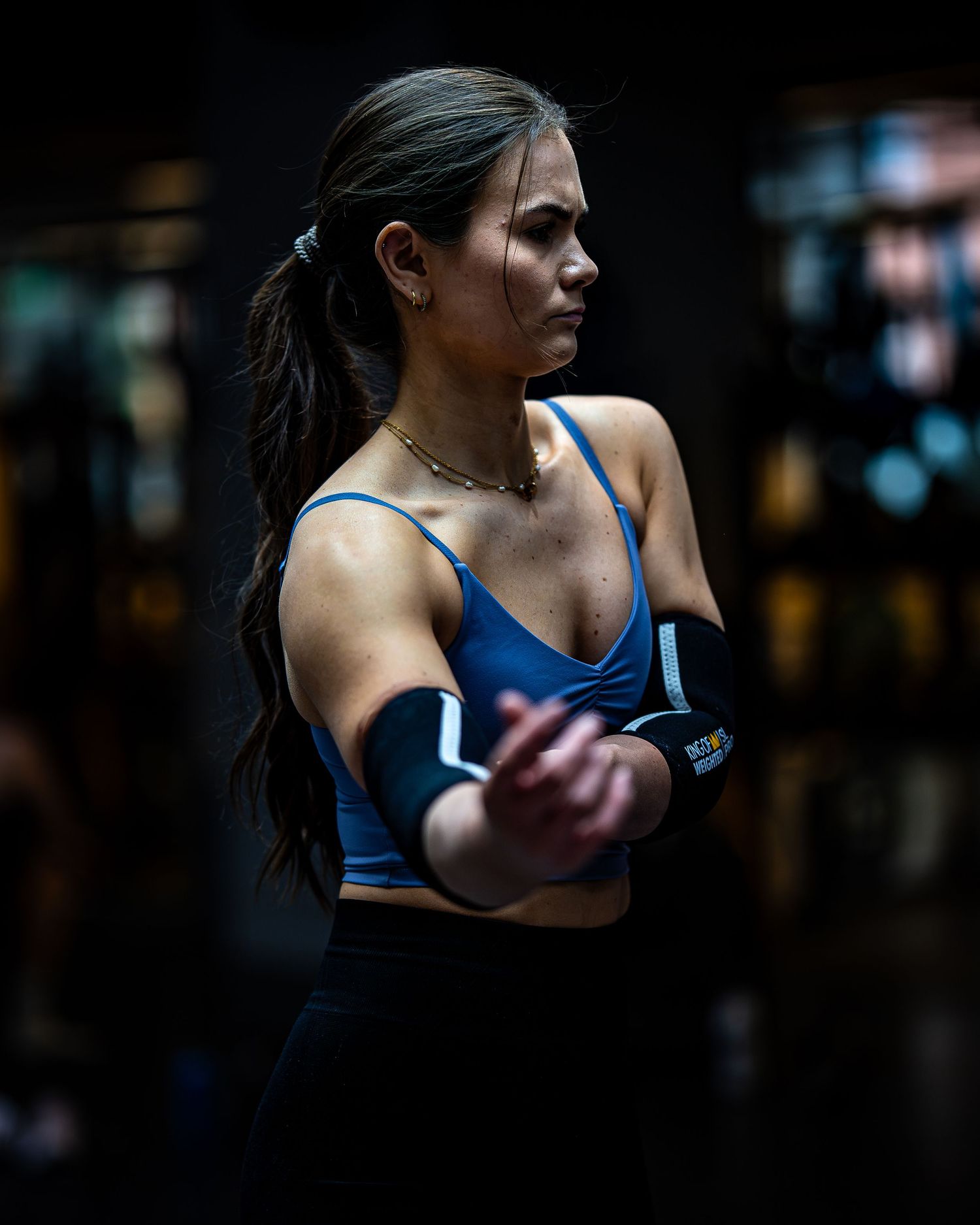 Athlete in blue sports bra focusing during workout in dimly lit gym environment.