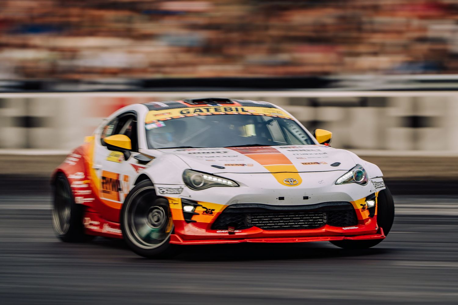 A Toyota GT86 race car drifting on a track with red and white livery and smoke trailing from its tires.
