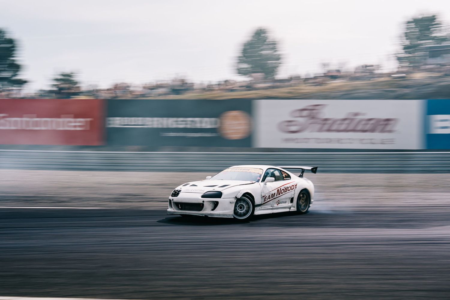 Multiple cars drift around a racetrack with motion blur creating a dynamic racing scene.