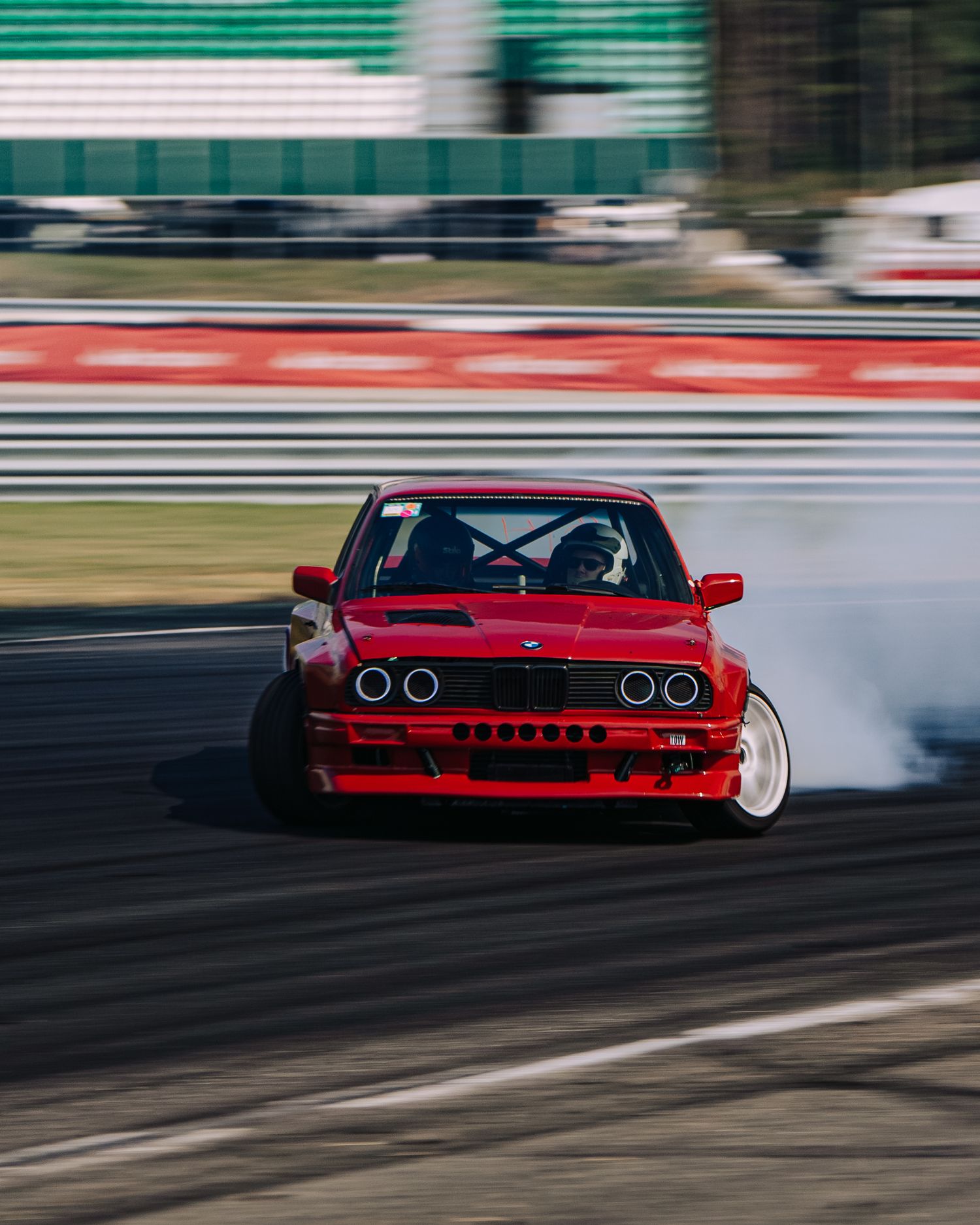 Red sports car drifting on a race track with motion blur and smoke trailing behind it.