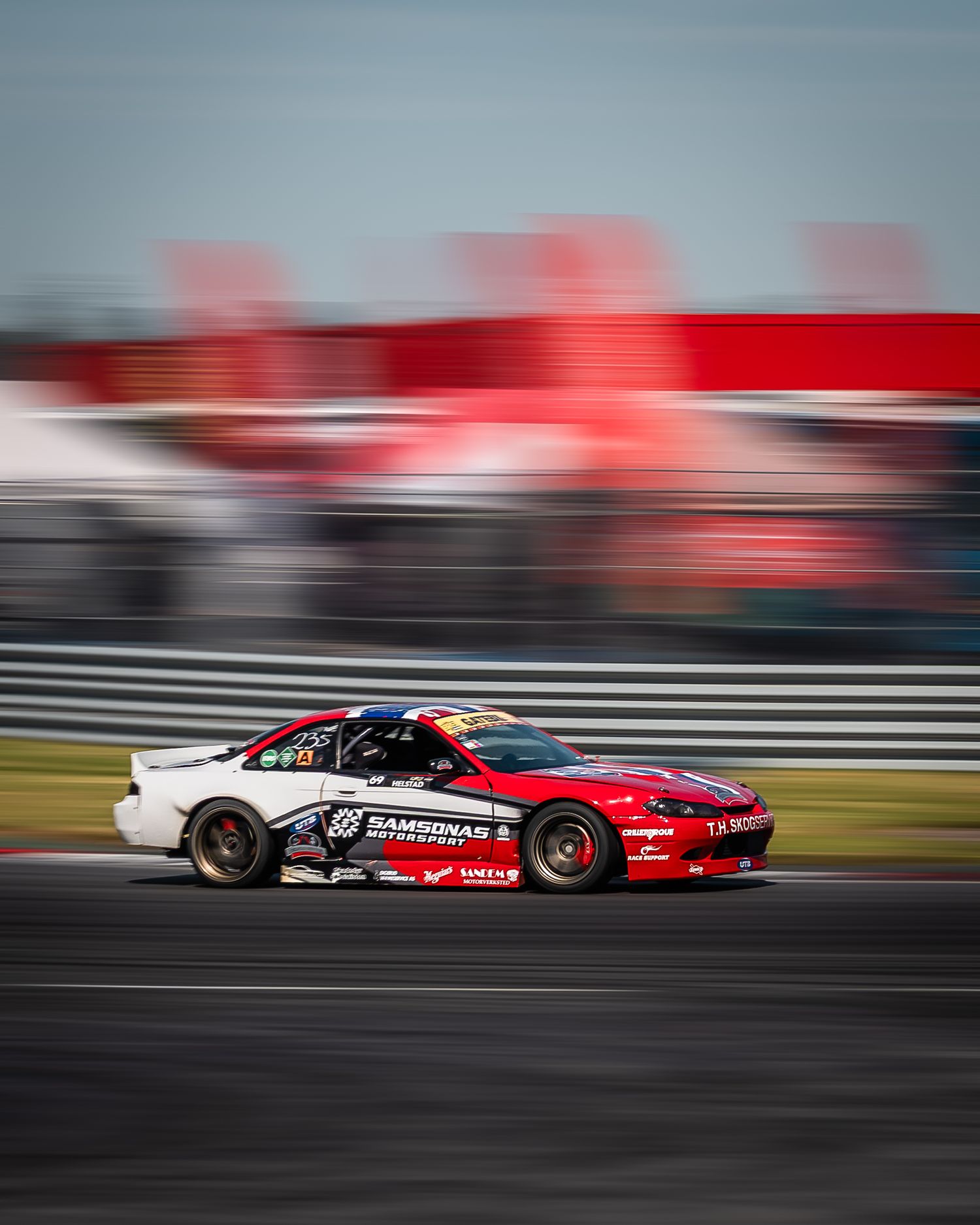 Red racing car speeding along racetrack with motion blur effect creating dynamic sense of movement and speed.