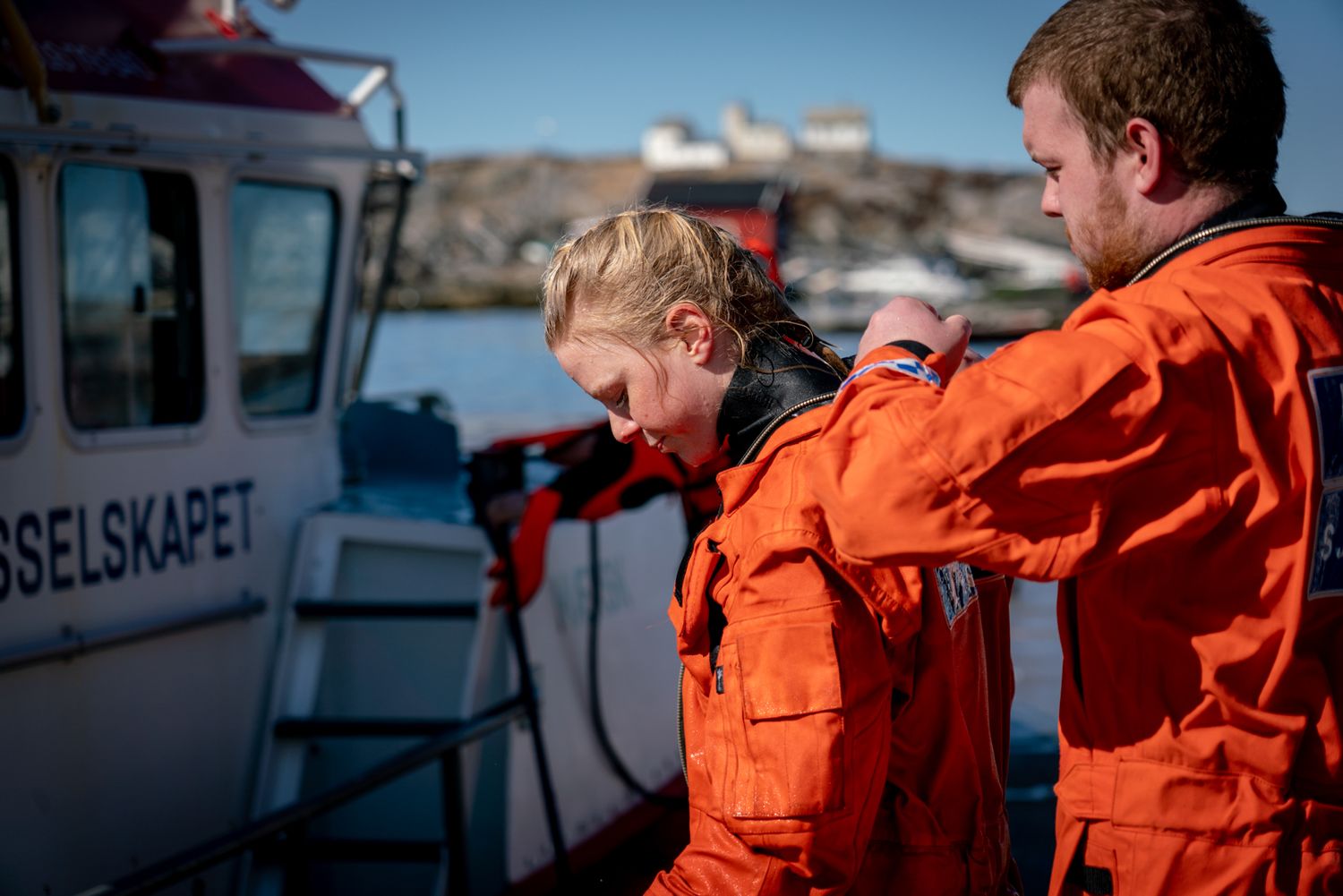 Rescue crew members in orange suits working on vessel deck.