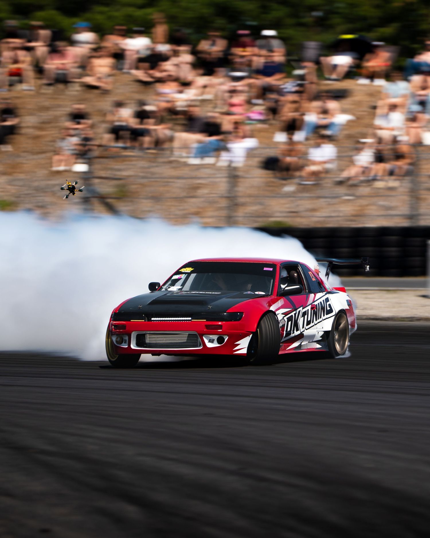 Red drift car creates smoke while sliding sideways on a race track during a drifting competition.