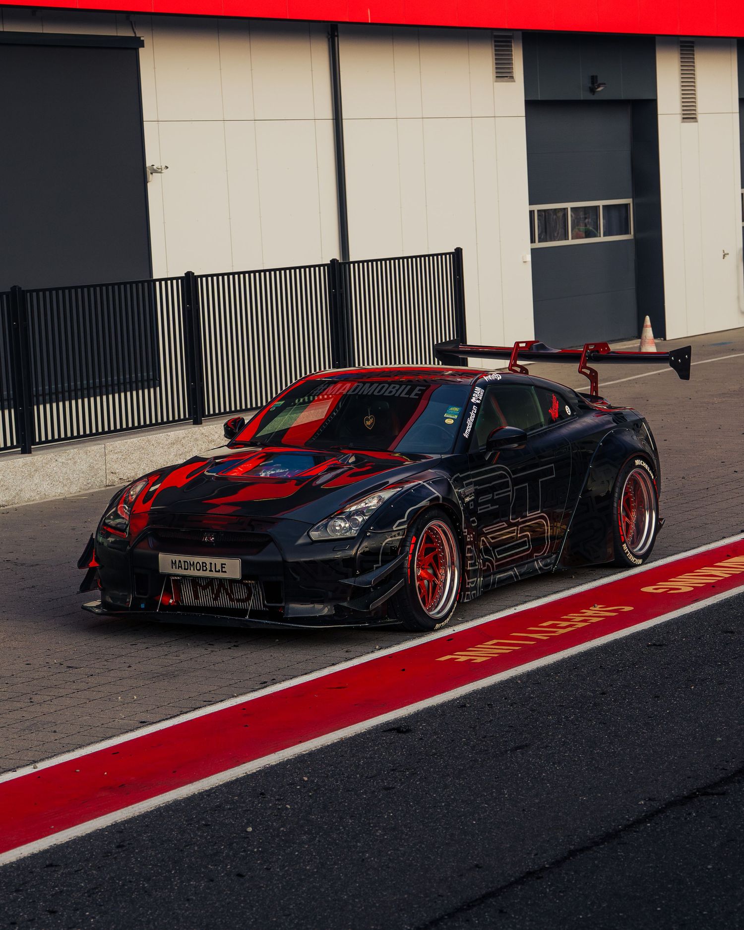 A black Nissan GT-R sports car with red accents and custom wheels parked on a track with red striping.