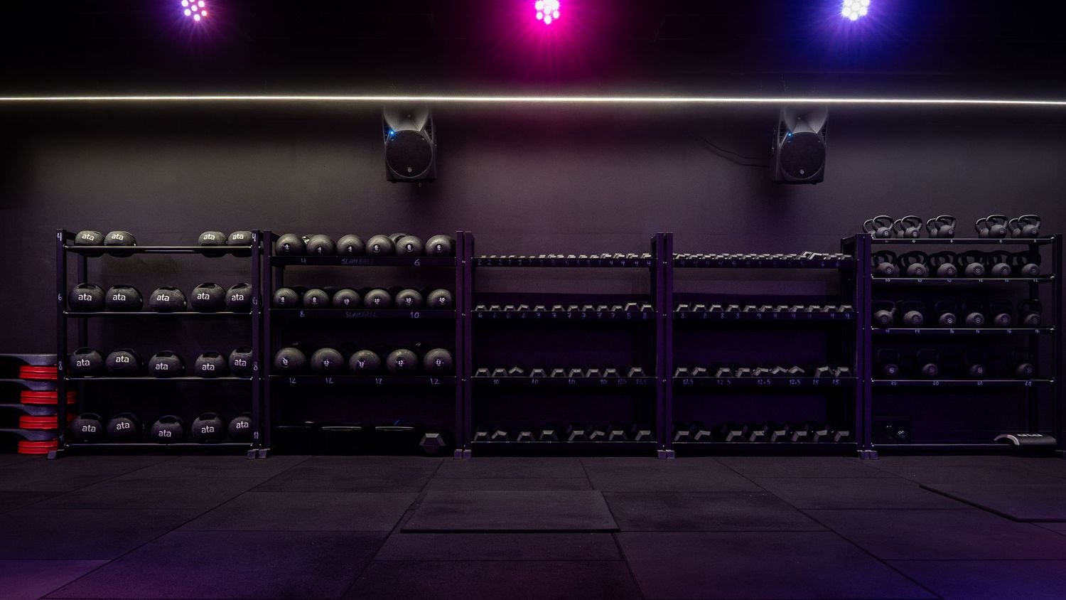 Row of colorful LED lights illuminate gym equipment in dark fitness studio.