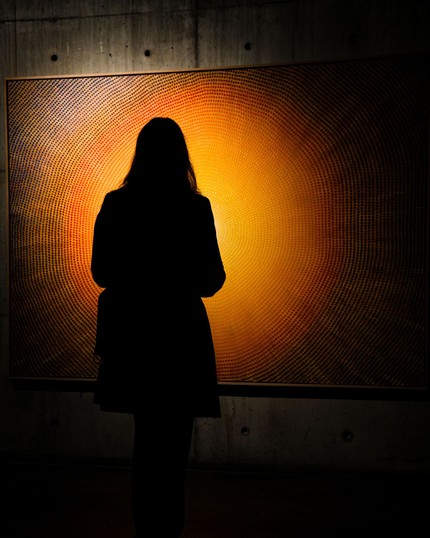 Silhouette of a figure standing before a glowing orange spiral artwork on a concrete wall.