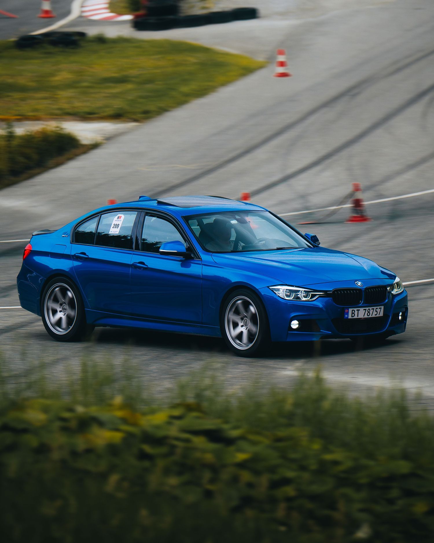 A sleek blue sports car navigates through orange traffic cones on a winding test track course.