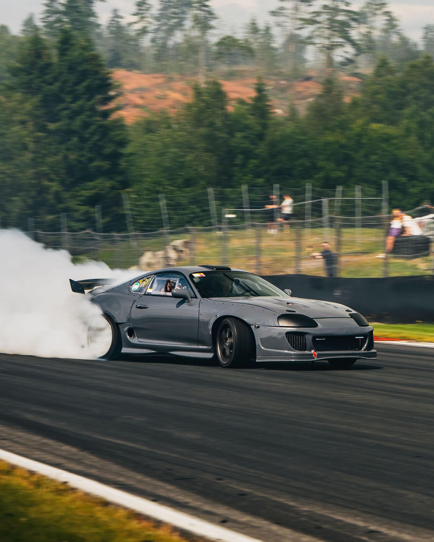 A silver sports car performs a dramatic drift on a racetrack with tire smoke billowing behind it.