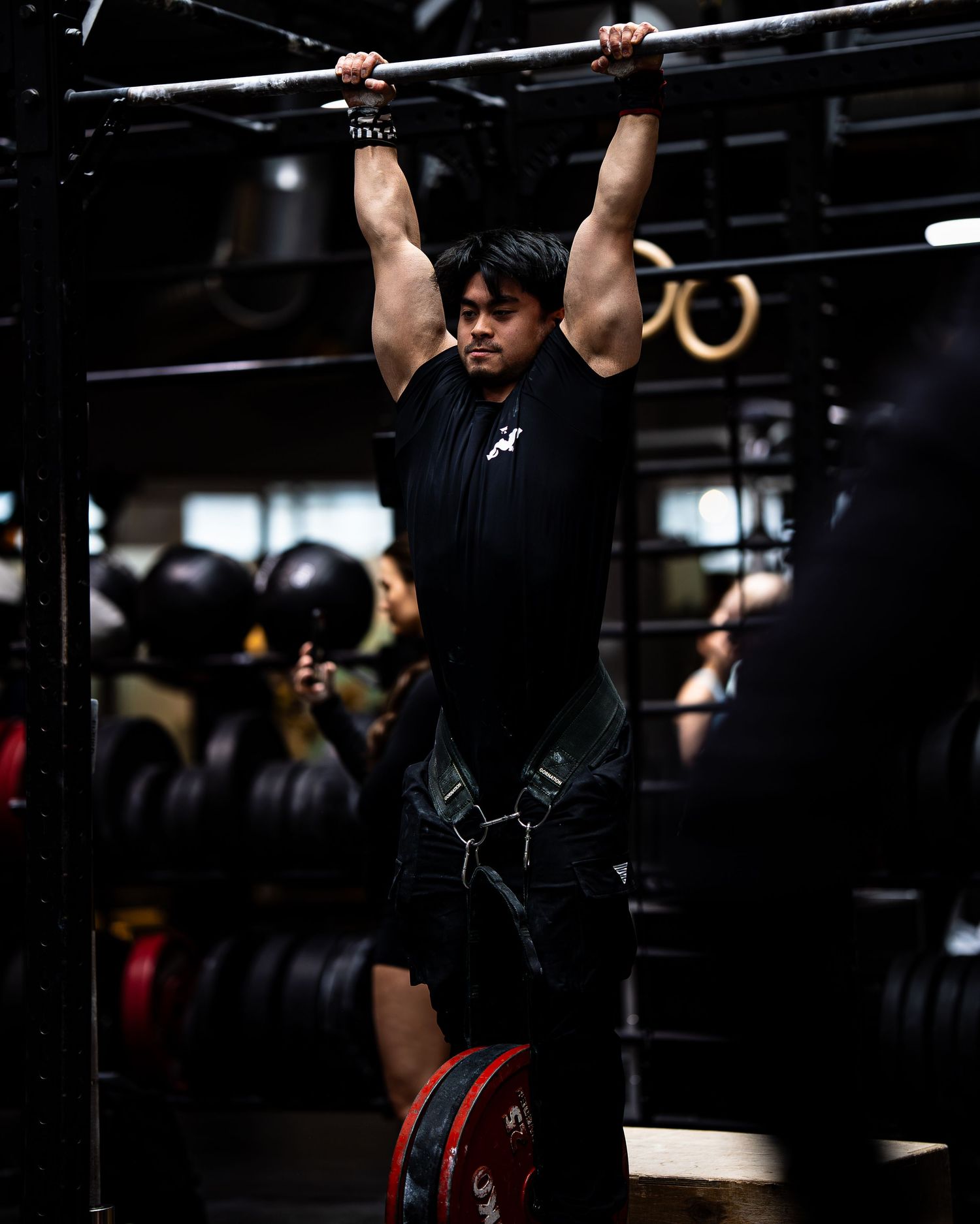 Athlete performing pull-ups at a CrossFit gym with weight plates visible in background.