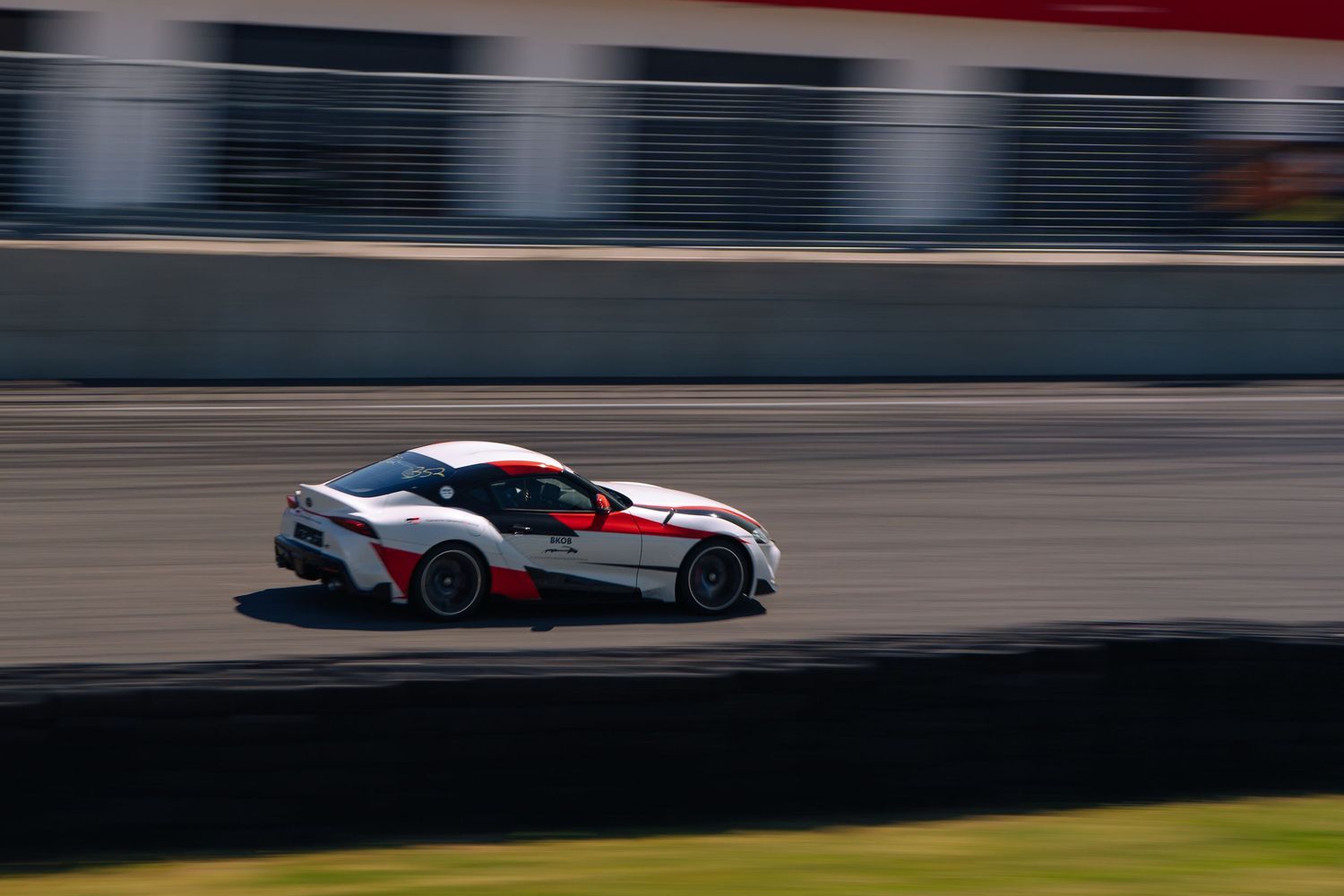 White racing car with distinctive livery navigates through a challenging race circuit corner at high speed.