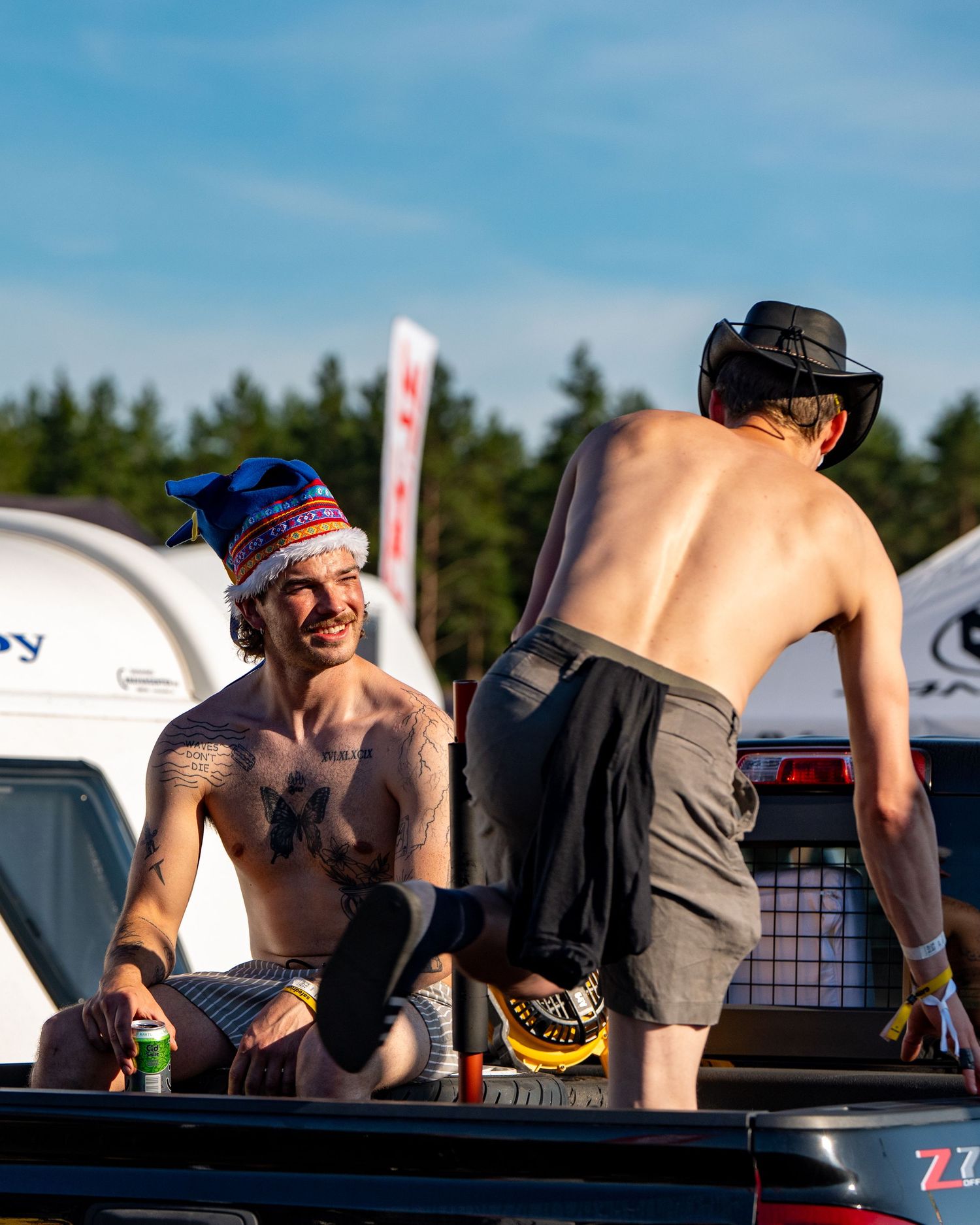 Athletes lean over pickup truck beds during an outdoor competition in sunny weather.