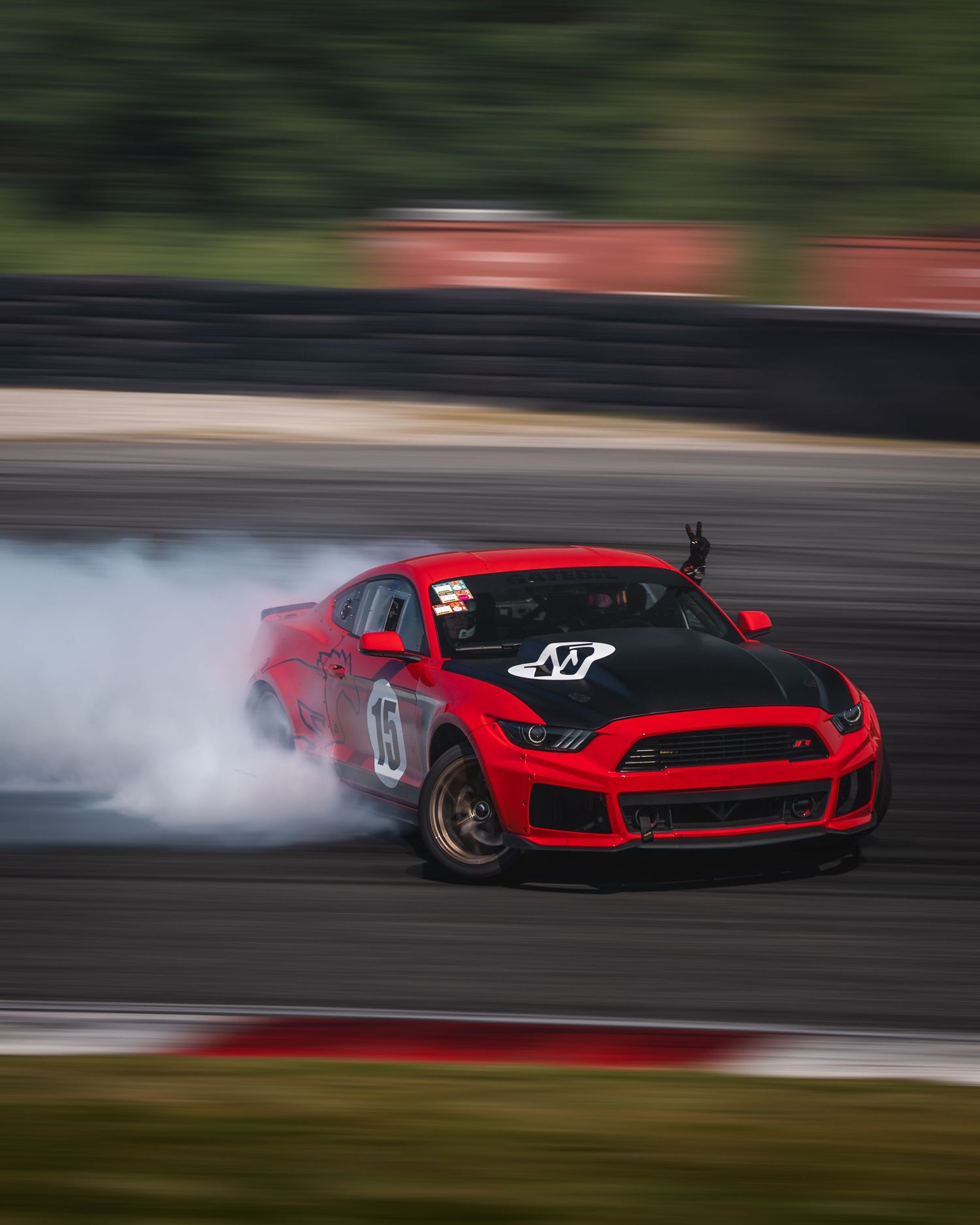 Red Ford Mustang drifting on a racetrack with smoke from burning tires during a motorsport competition.