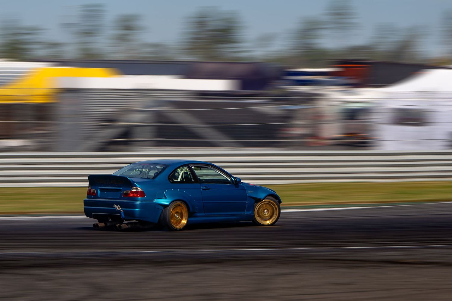A blue sports car drifts sideways on a race track with smoke billowing from its tires during a drift competition.