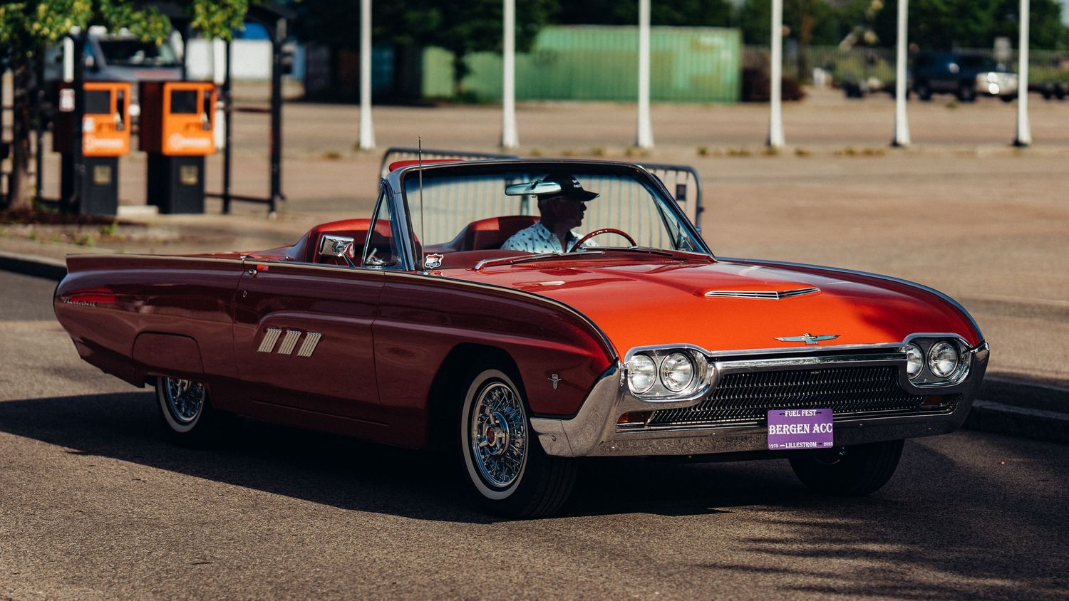 Orange vintage Thunderbird convertible with classic fins and chrome details parked outdoors.