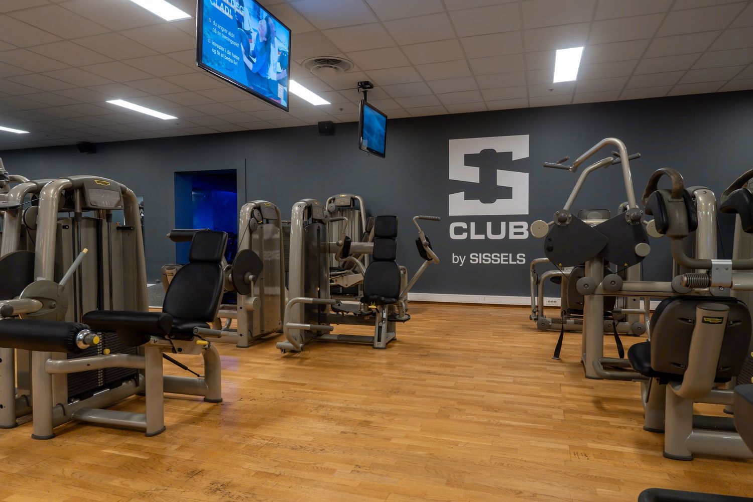 Fitness center with wood flooring and modern resistance training machines.