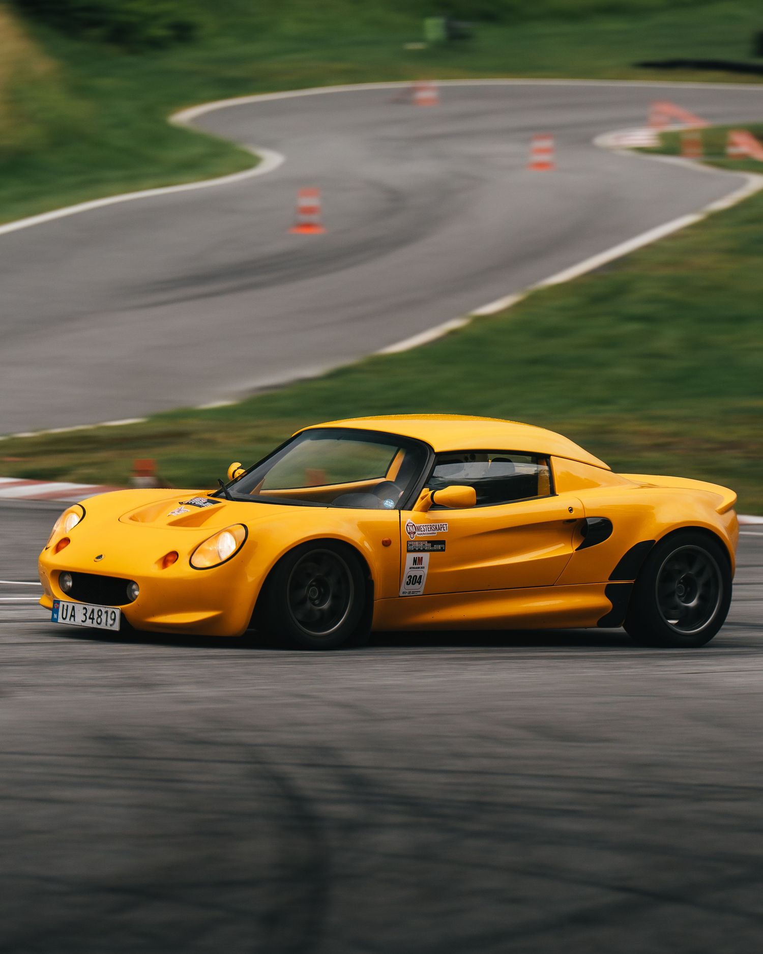 A bright yellow sports car drifting sideways on a racetrack with orange cones visible in the background.