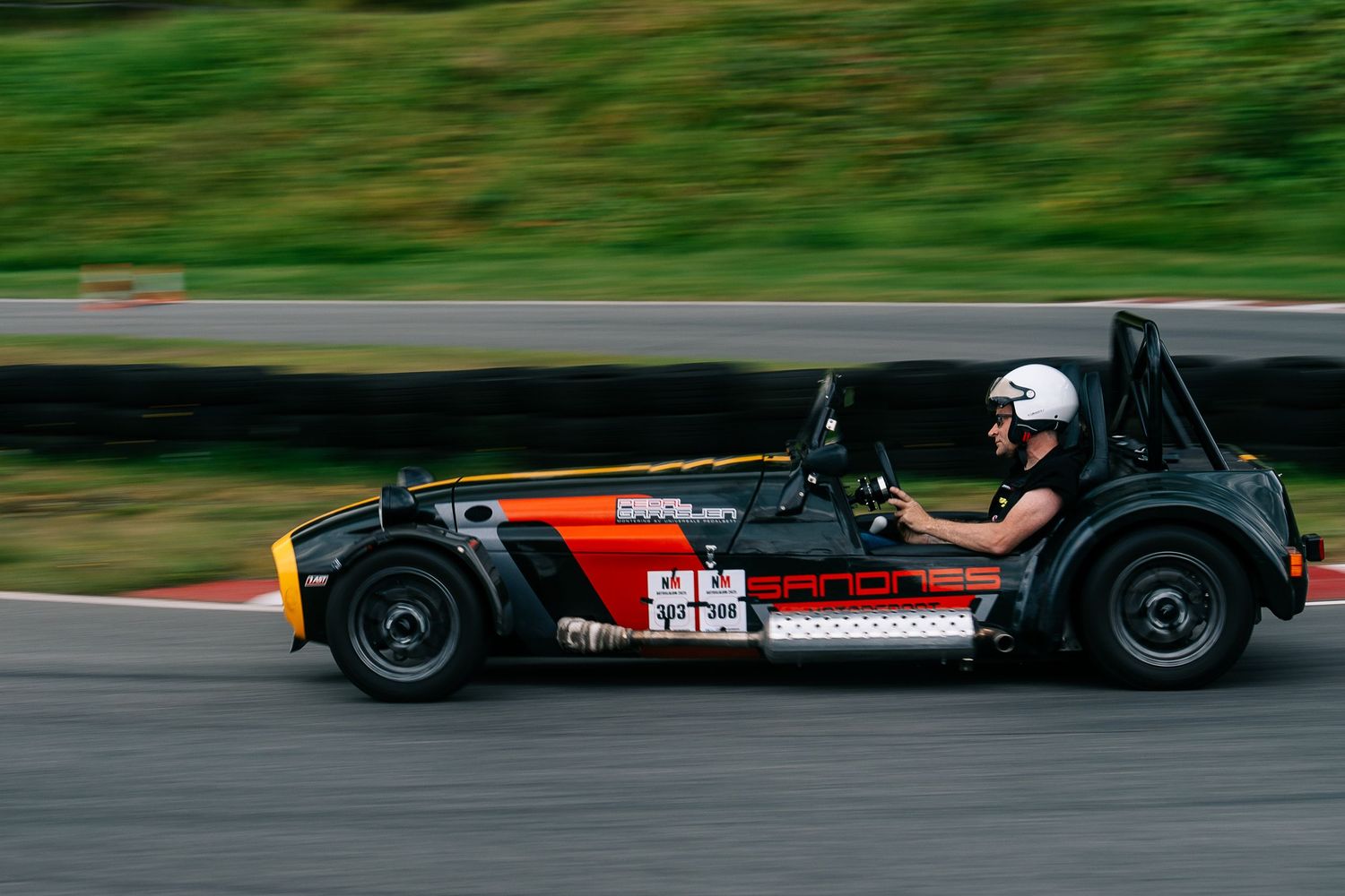 Red and black race cars compete on a green racetrack during a motorsport competition.