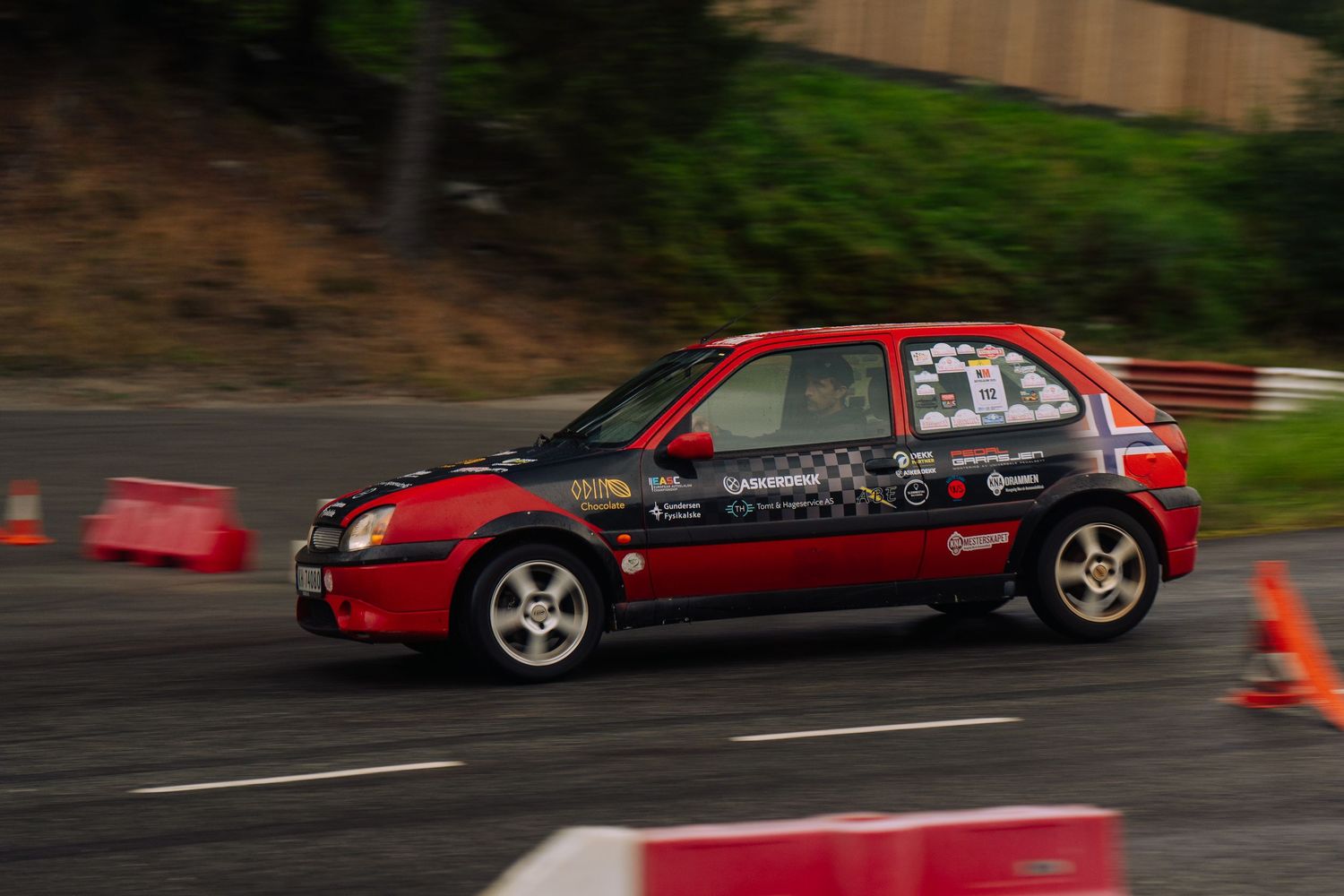 Red and black race cars navigate through a winding track during a drift competition event.