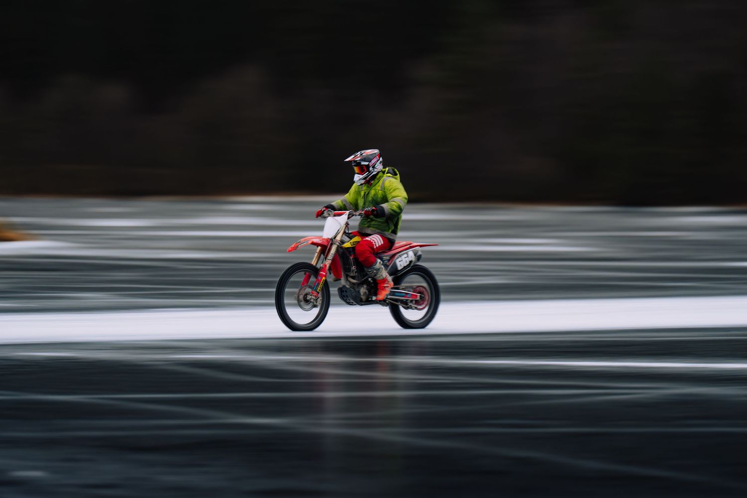 A red motorcycle speeds across a snowy winter landscape creating a motion blur effect against the white background.