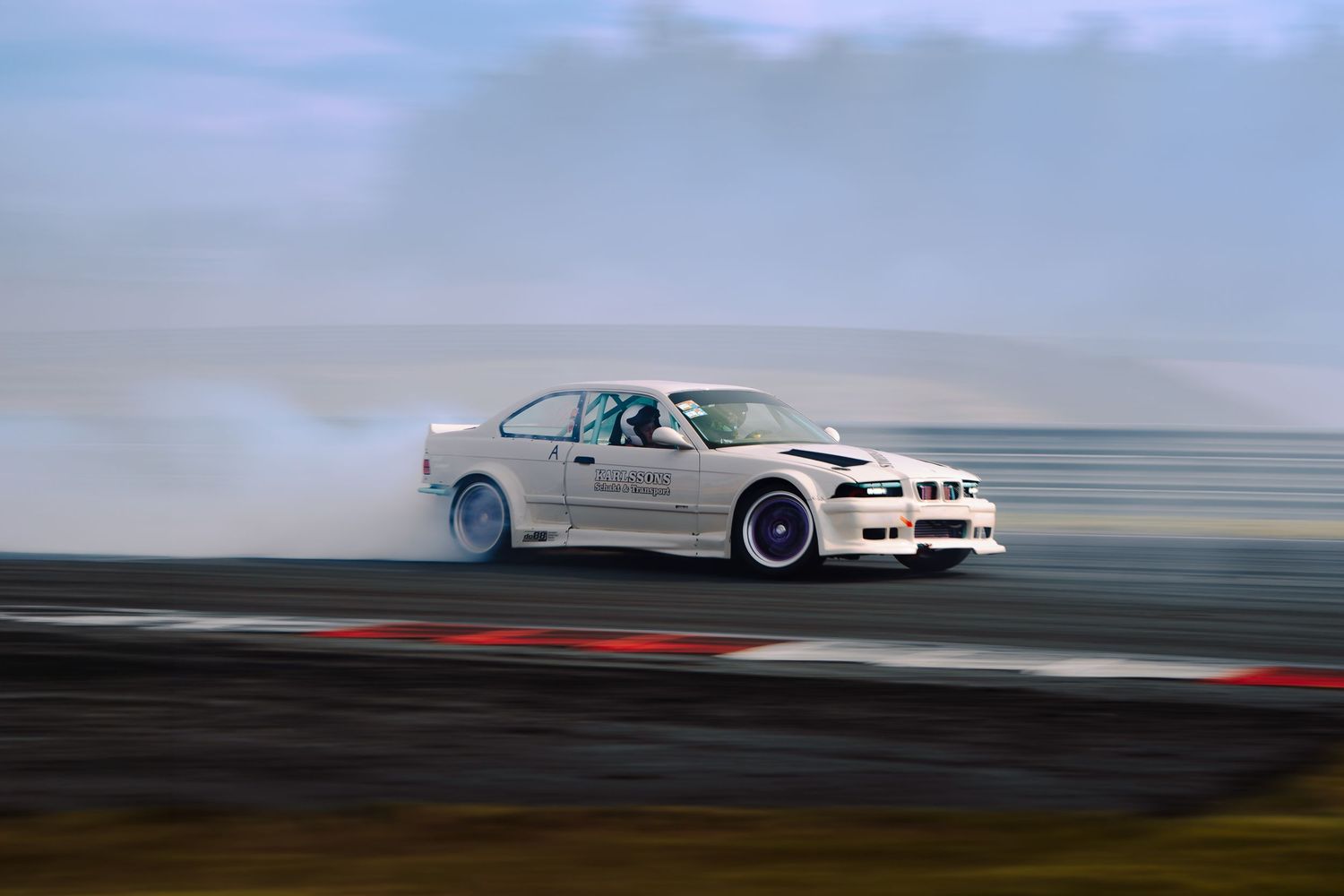 A white BMW drifting on a racetrack with tire smoke trailing behind it.