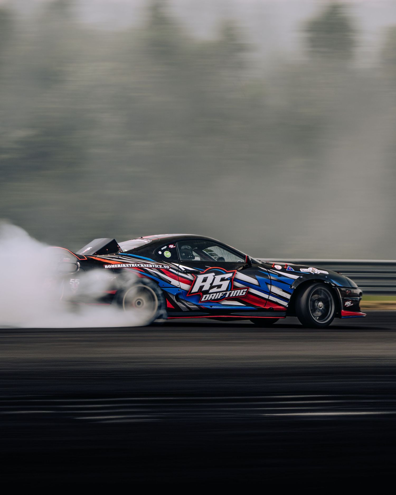 A race car drifting on a track with smoke billowing from its tires while performing a controlled slide.