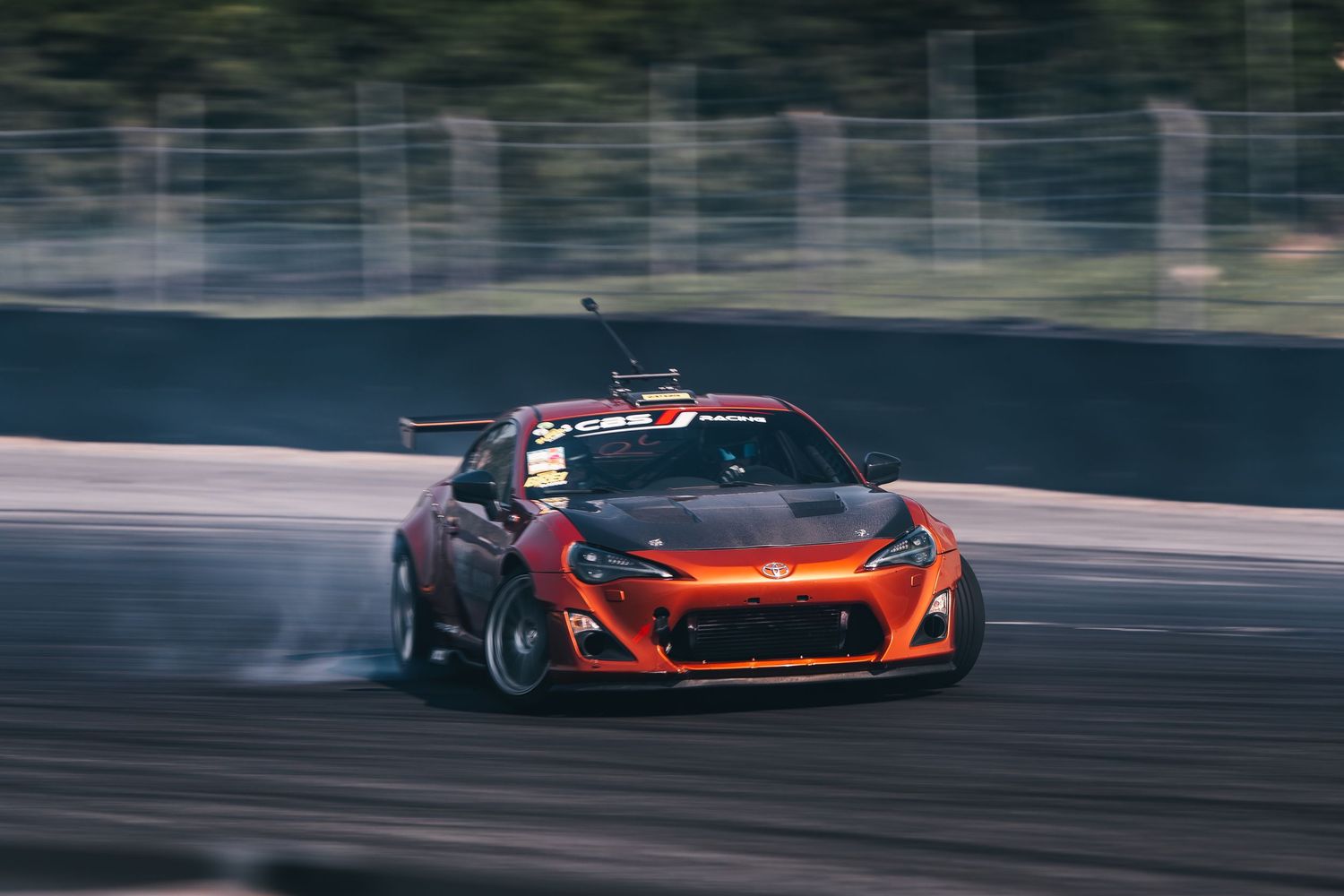 Orange McLaren supercar drifting on a racetrack with smoke trailing from its tires during high-speed cornering.