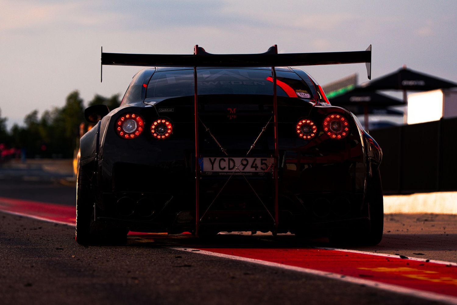Black racing car with glowing red taillights seen from behind on a racetrack at dusk.