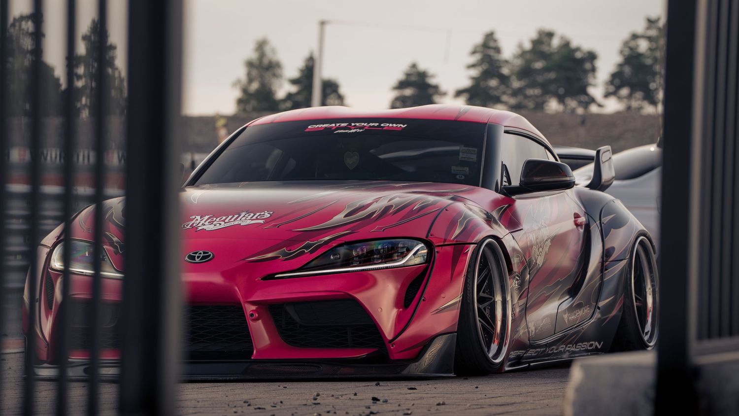 Modified pink Toyota Supra with wide body kit and aggressive aerodynamics parked on street at dusk.