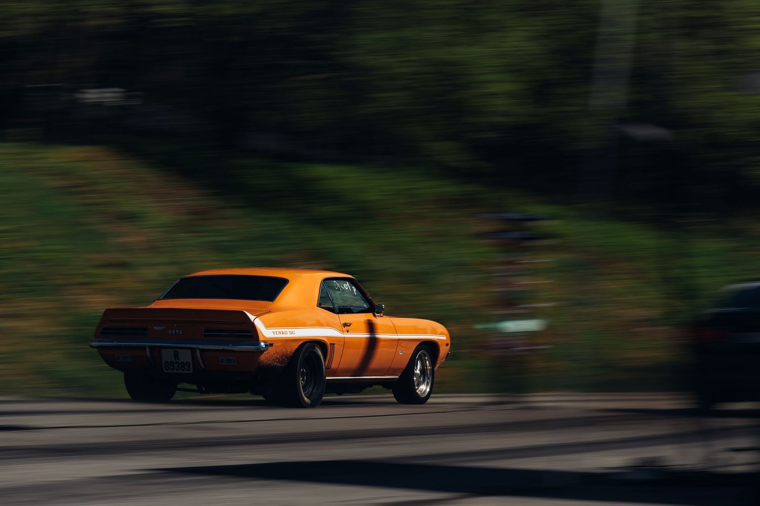 Cinematic sequence showing an orange classic muscle car driving on a winding forest road.