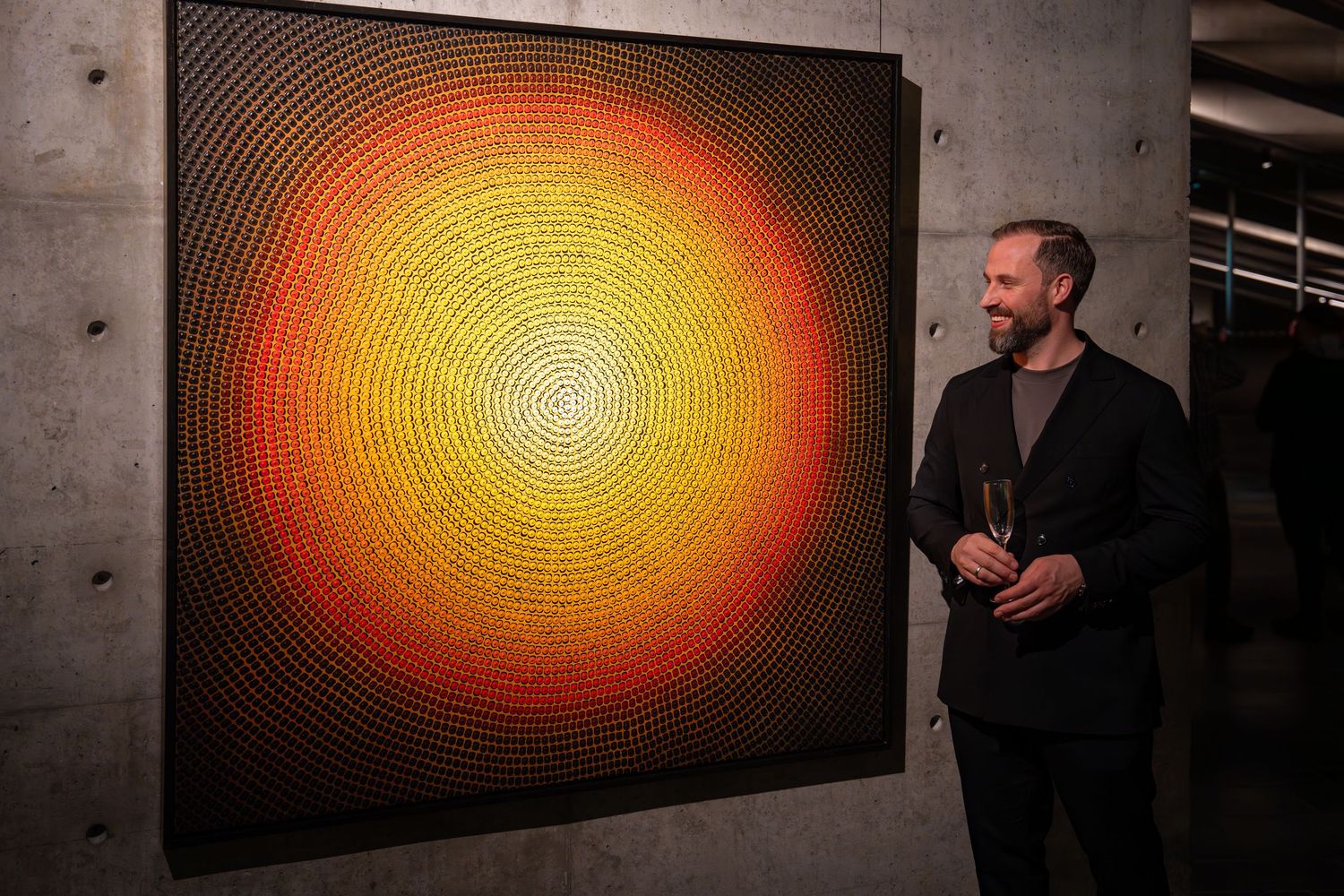 Large orange spiral artwork displayed on concrete wall in contemporary gallery setting.