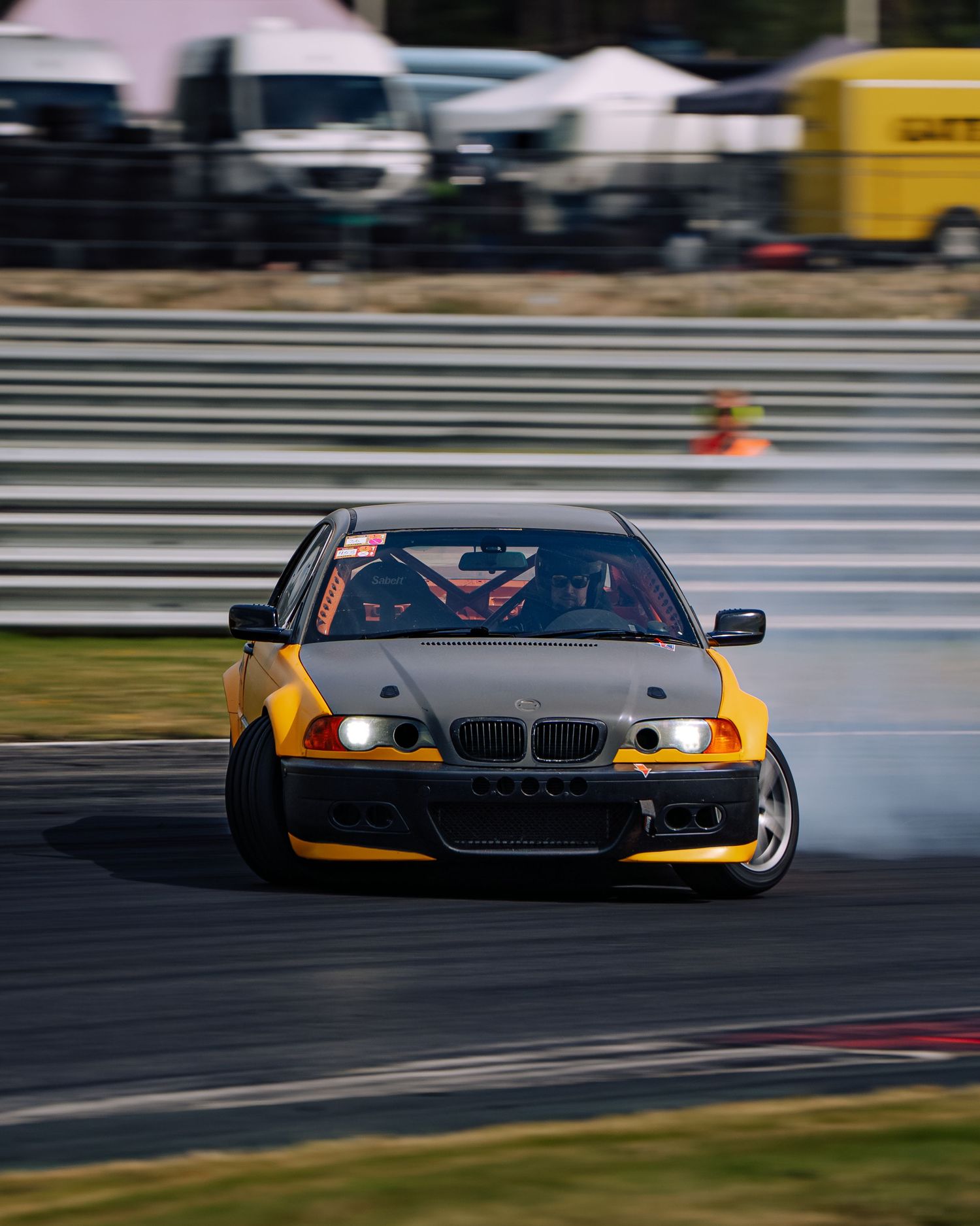 A black and yellow BMW race car drifts sideways on a racetrack with motion blur and smoke from the tires.