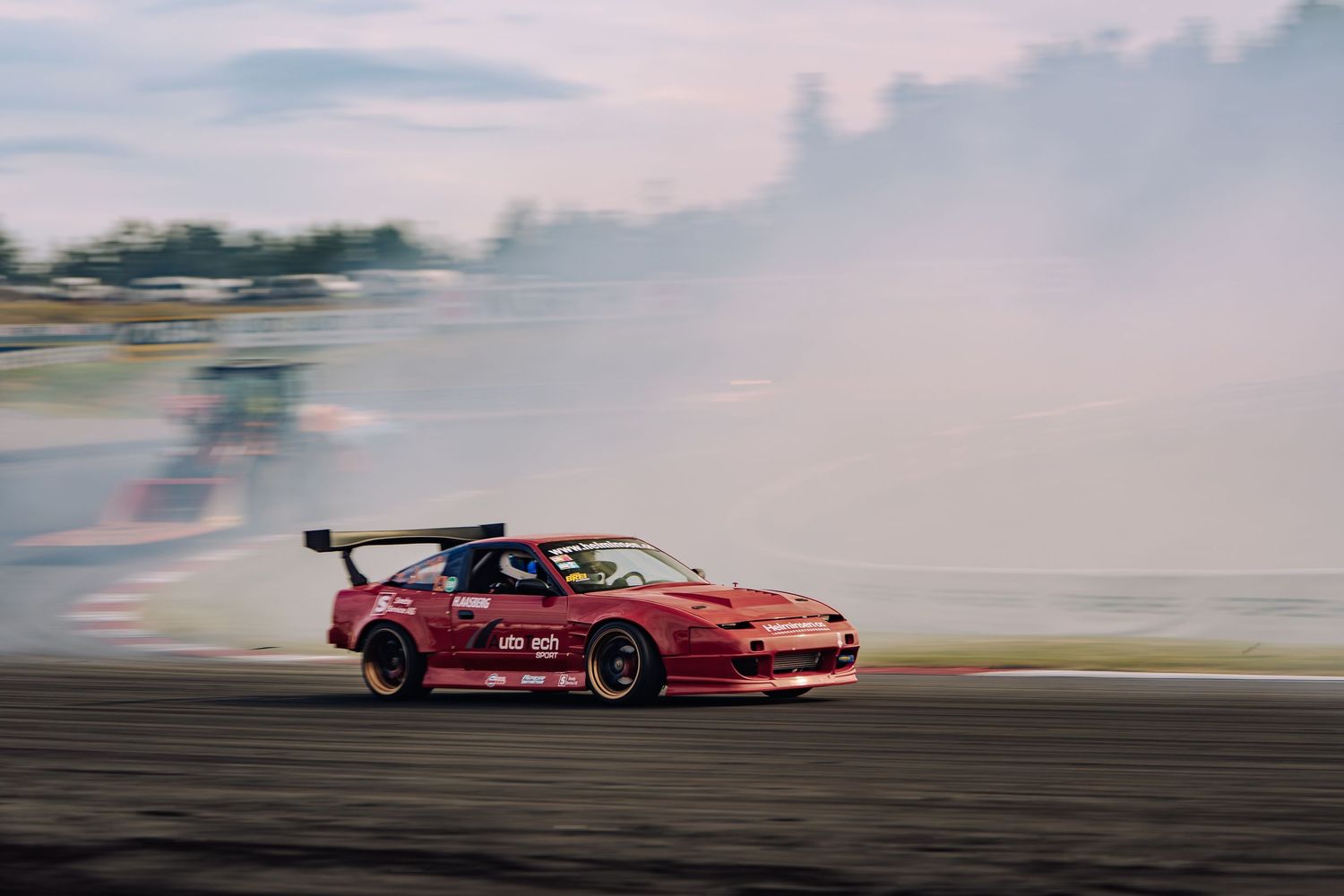 Red sports car drifting on a racetrack with smoke trailing behind during a motorsport competition.