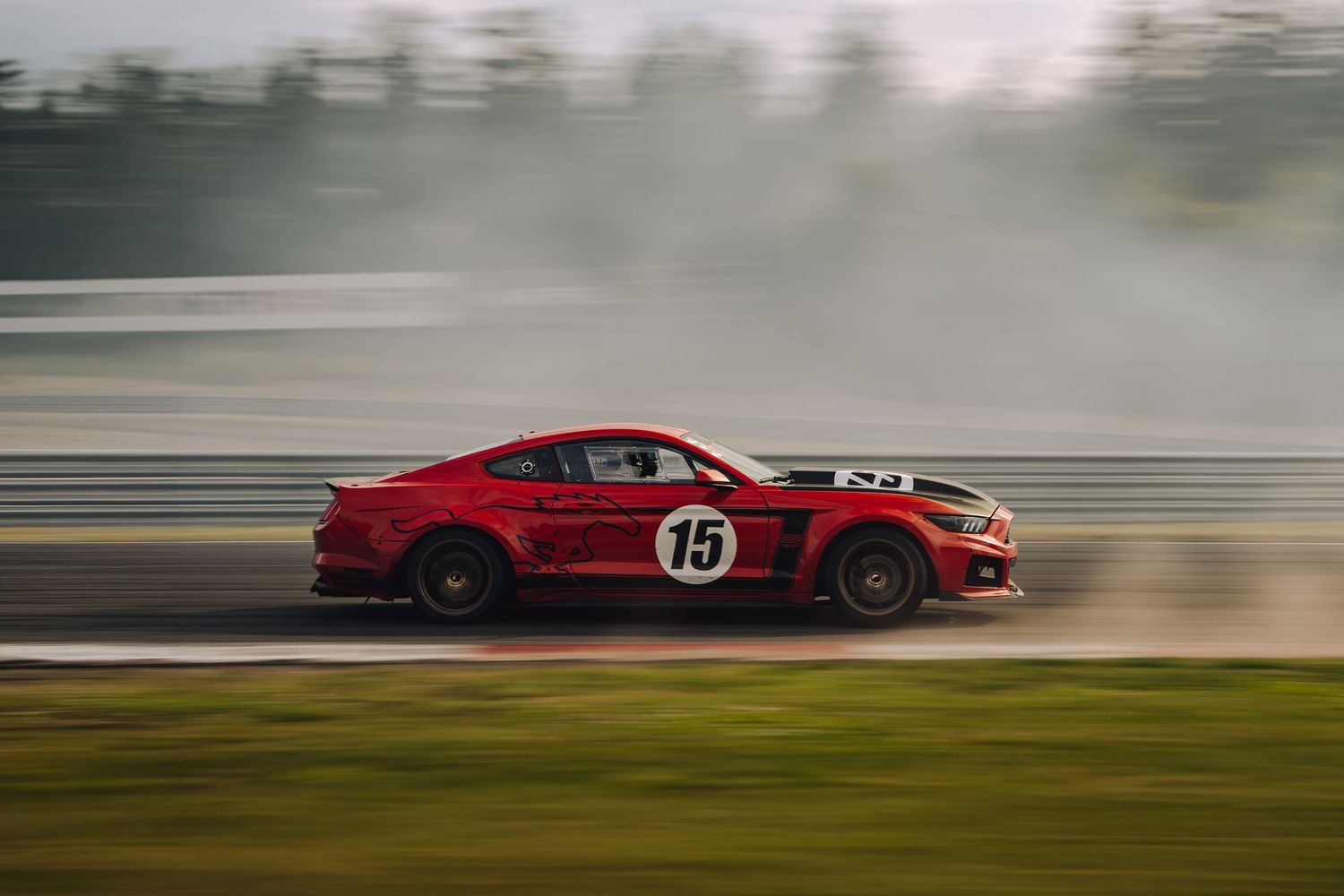 A red race car drifts sideways on a racetrack creating smoke from its tires during a motorsport competition.