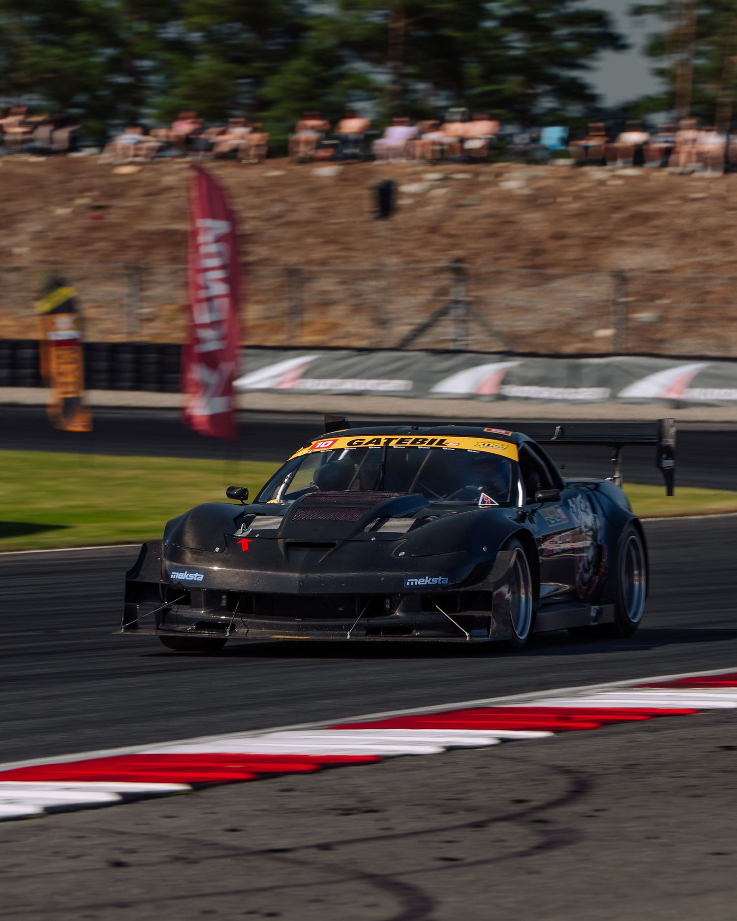 Black racing car navigates a curve on racetrack with red and white curbing during motorsport competition.