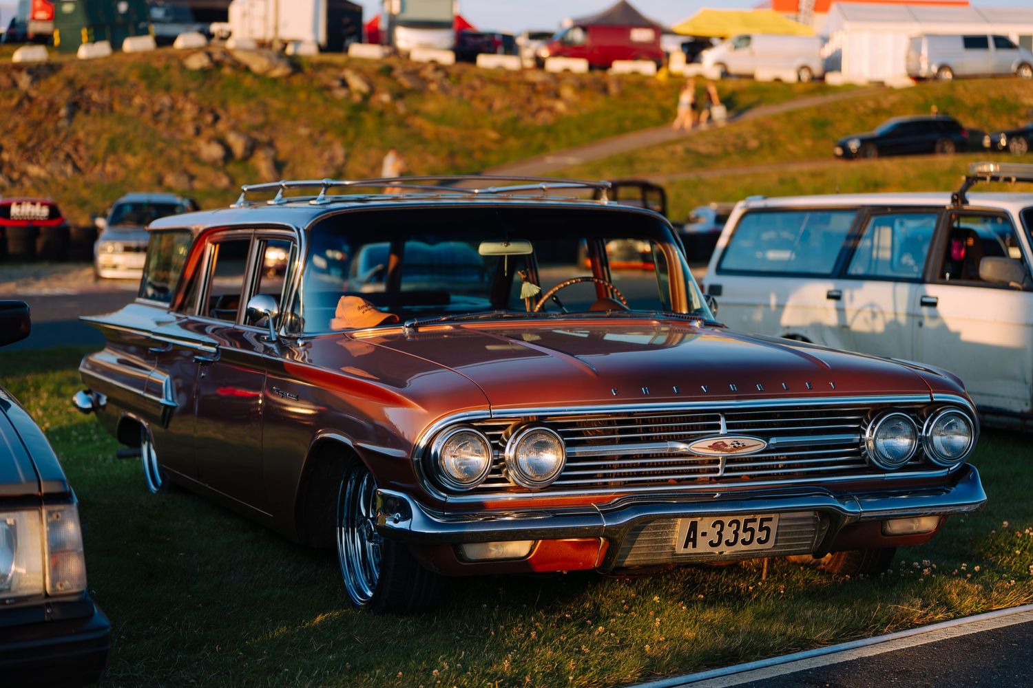 Classic Chevrolet Impala cars lined up at sunset during a vintage automobile show displaying their iconic designs.