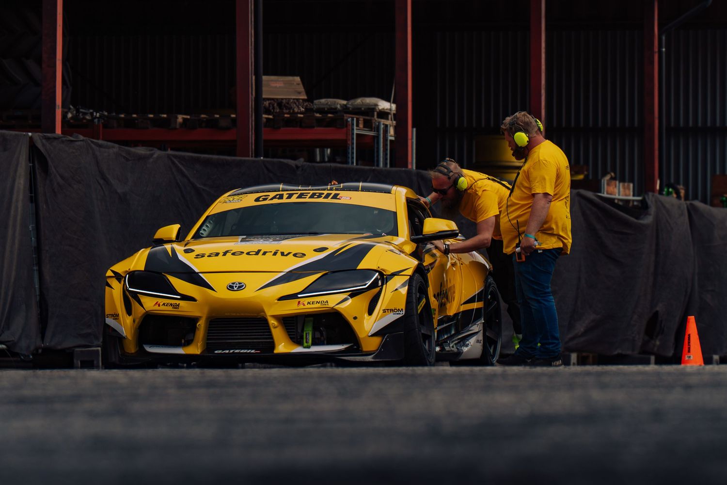Yellow McLaren sports cars parked at a track event with orange traffic cones in the background.