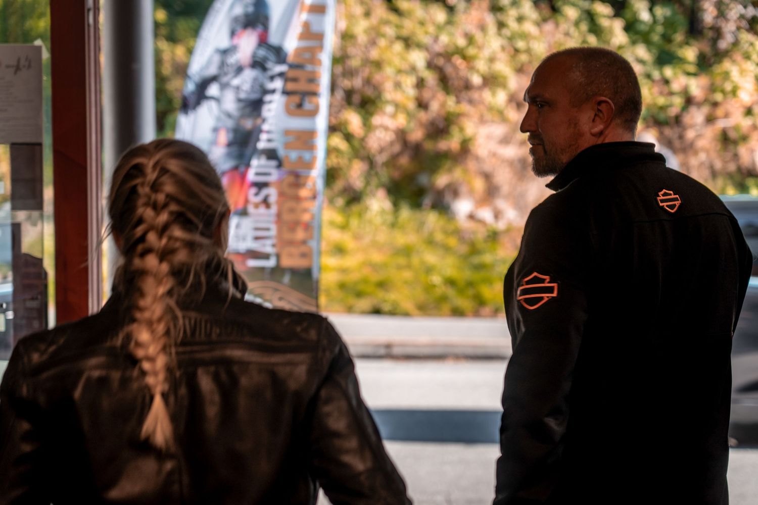 Silhouettes in leather jackets stand outside in autumn lighting during a motorcycle meetup.