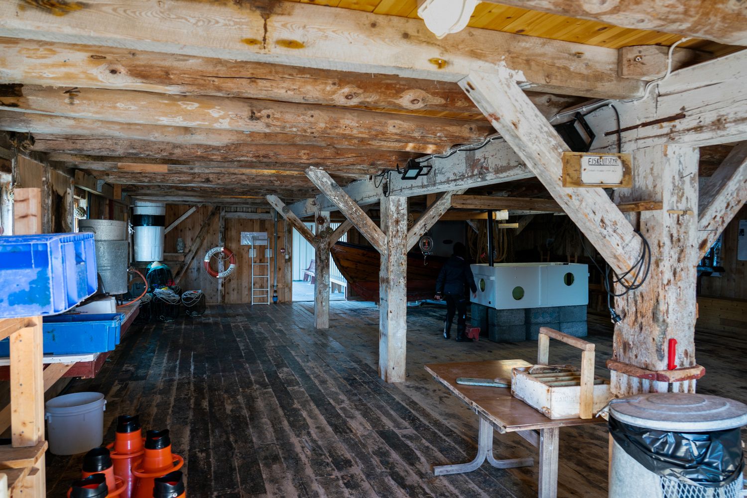 Interior of rustic wooden boathouse with exposed beams and maritime equipment.