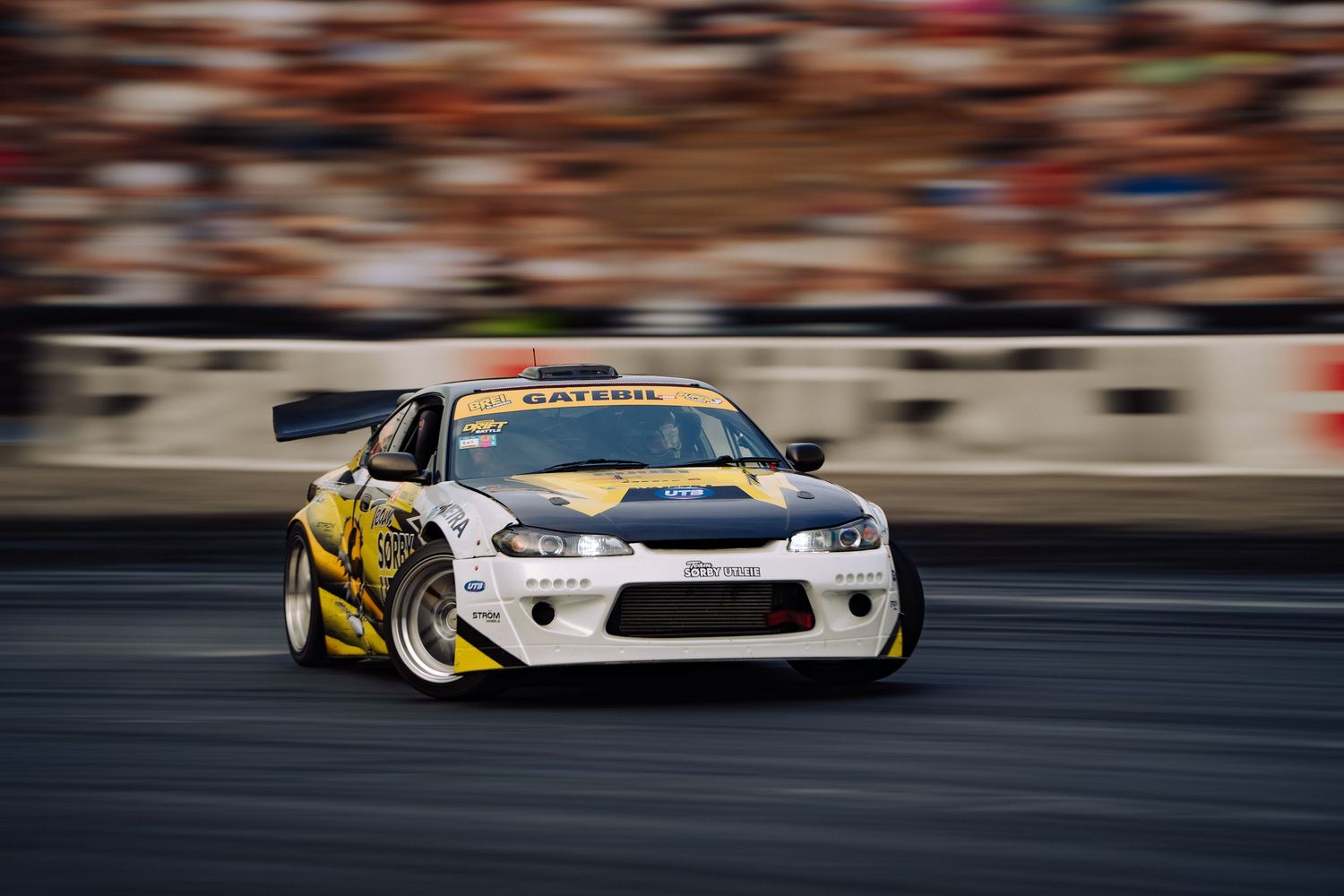 Modified drift car with yellow accents performing a drift maneuver on a race track.