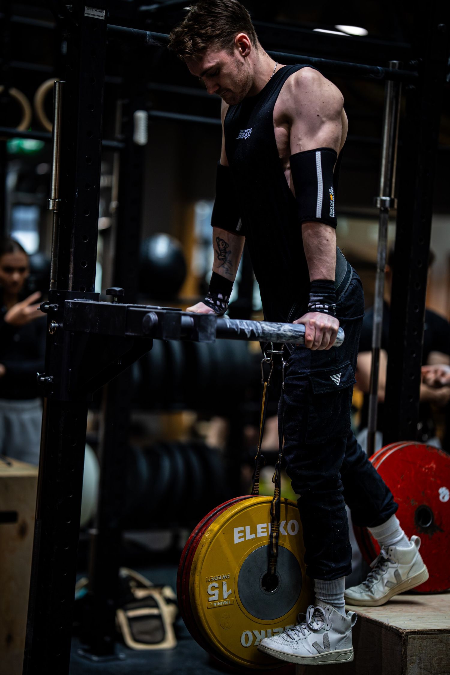 Athlete performing dips on parallel bars with yellow Eleiko weight plate visible in dark gym setting.